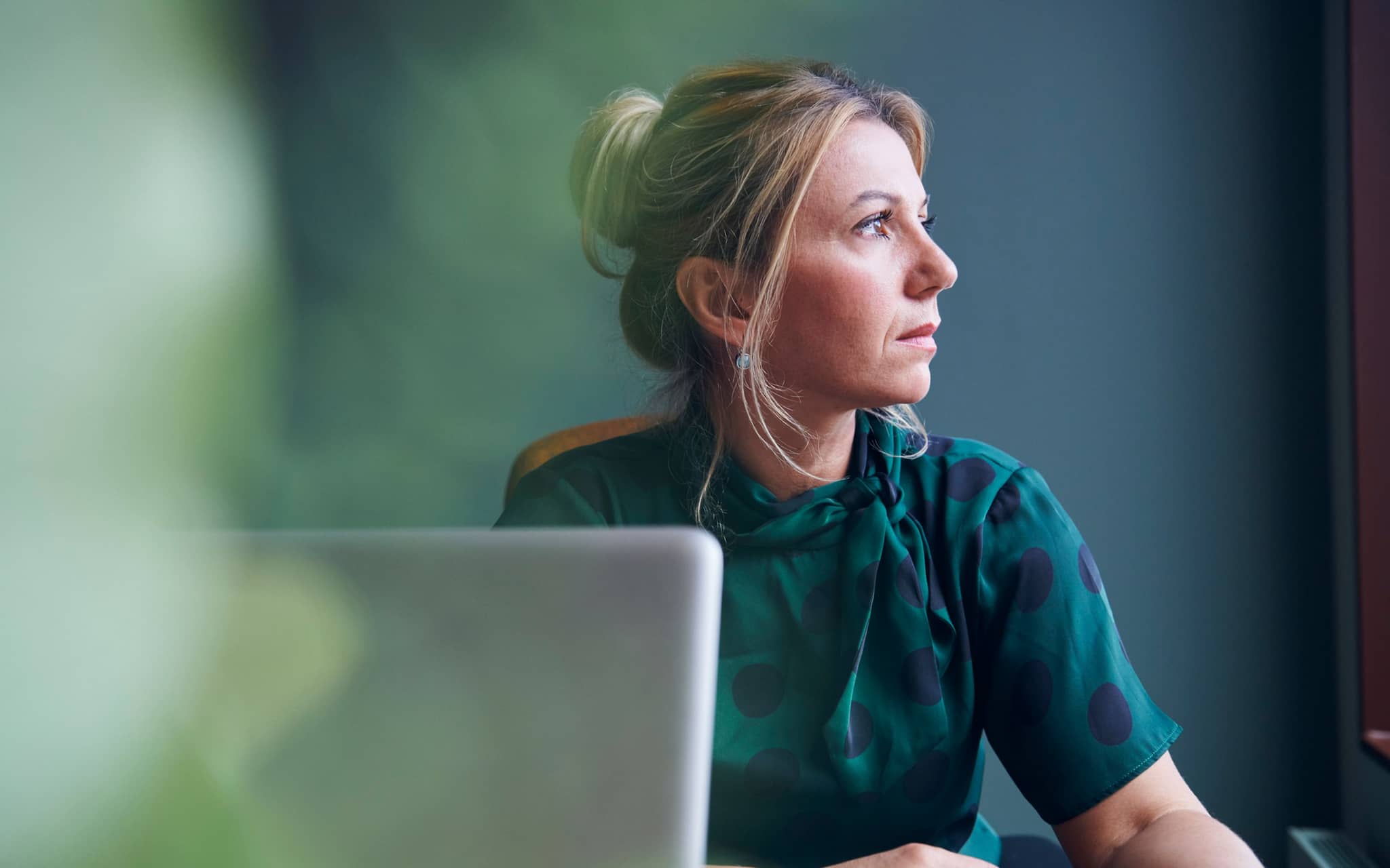 Hochfunktionale Depression: Gepflegte Frau vor einem PC schaut traurig zur Seite.