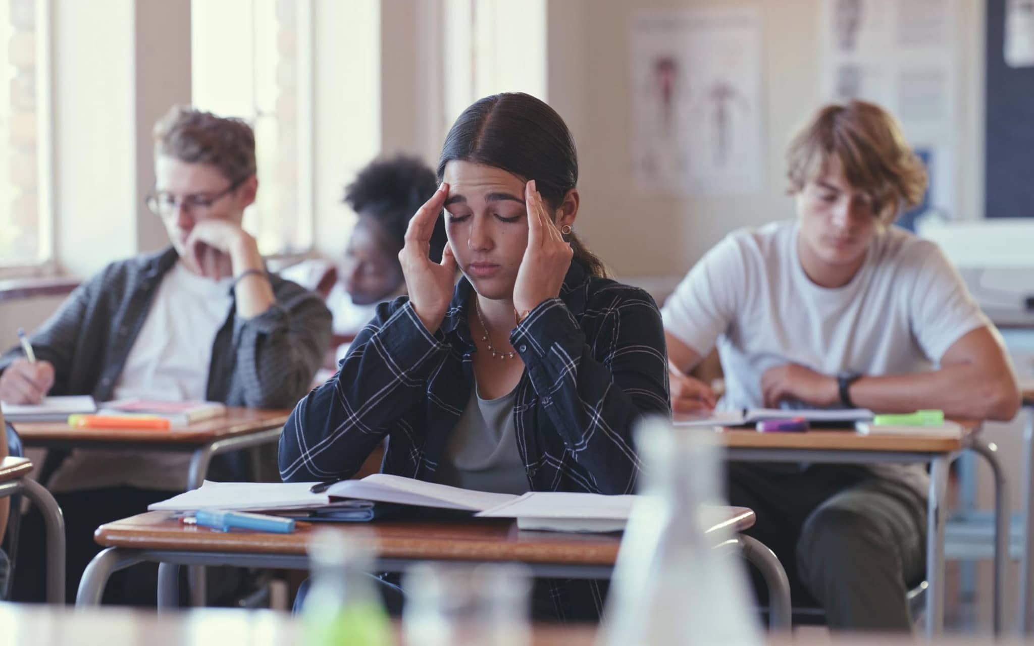 Präventionsradar 2025: Teenagerin sitzt mit geschlossenen Augen in der Schulklasse und hält sich die Hände an die Schläfen.