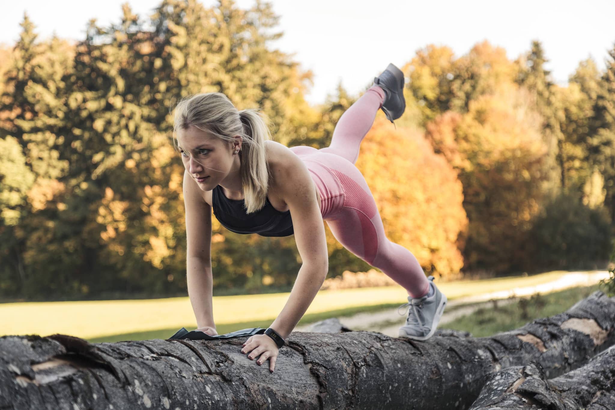Junge Frau macht Liegestützte auf einem Baumstamm in der Natur.