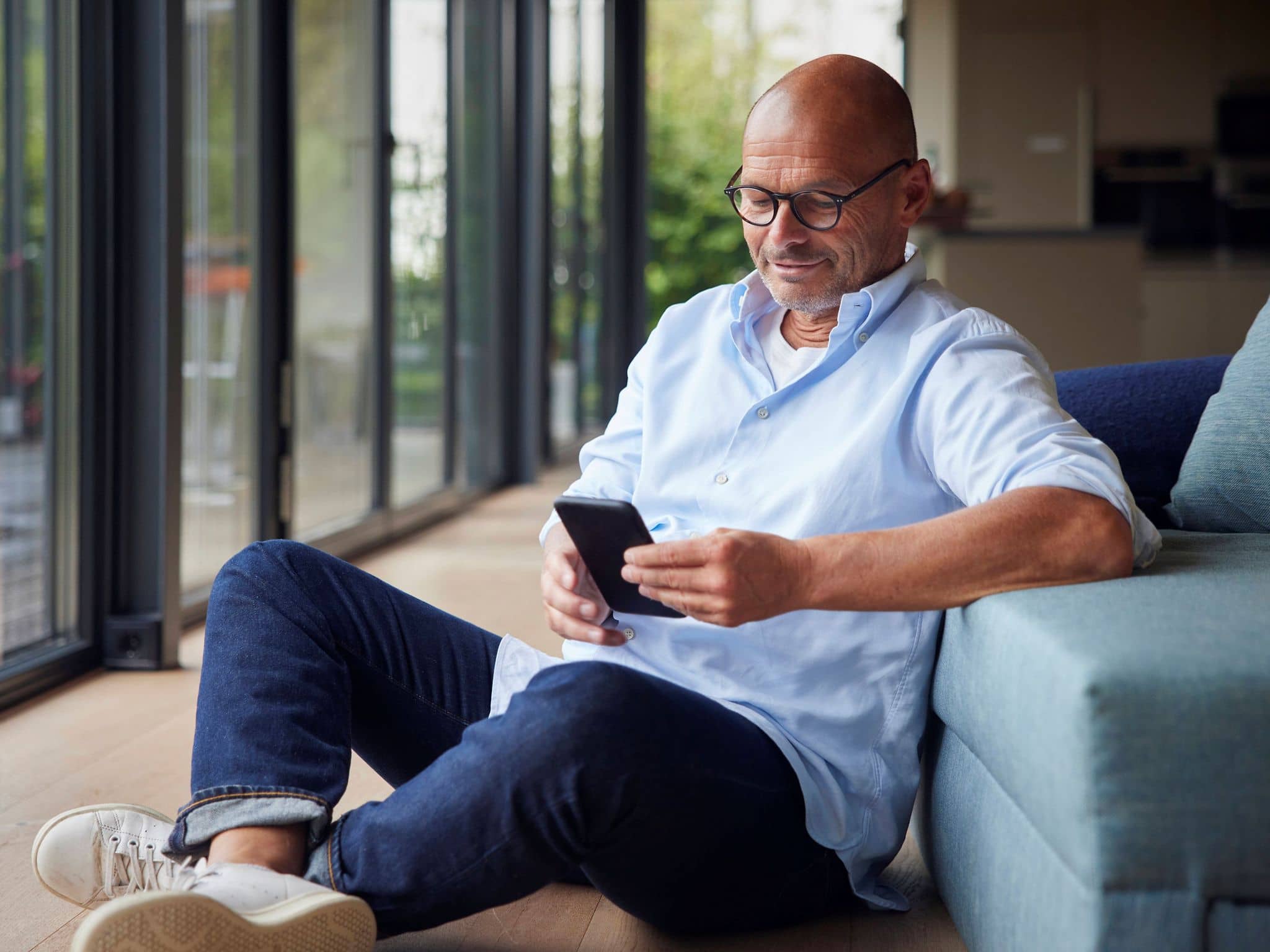 Ein älterer Mann sitzt im Wohnzimmer und schaut auf sein Handy.