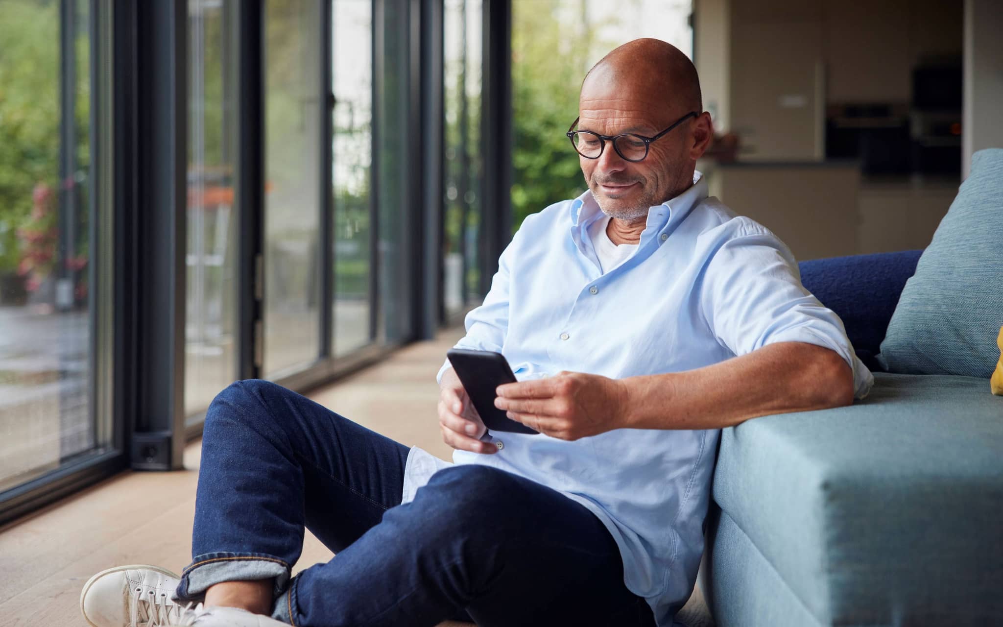 Ein älterer Mann sitzt im Wohnzimmer und schaut auf sein Handy.