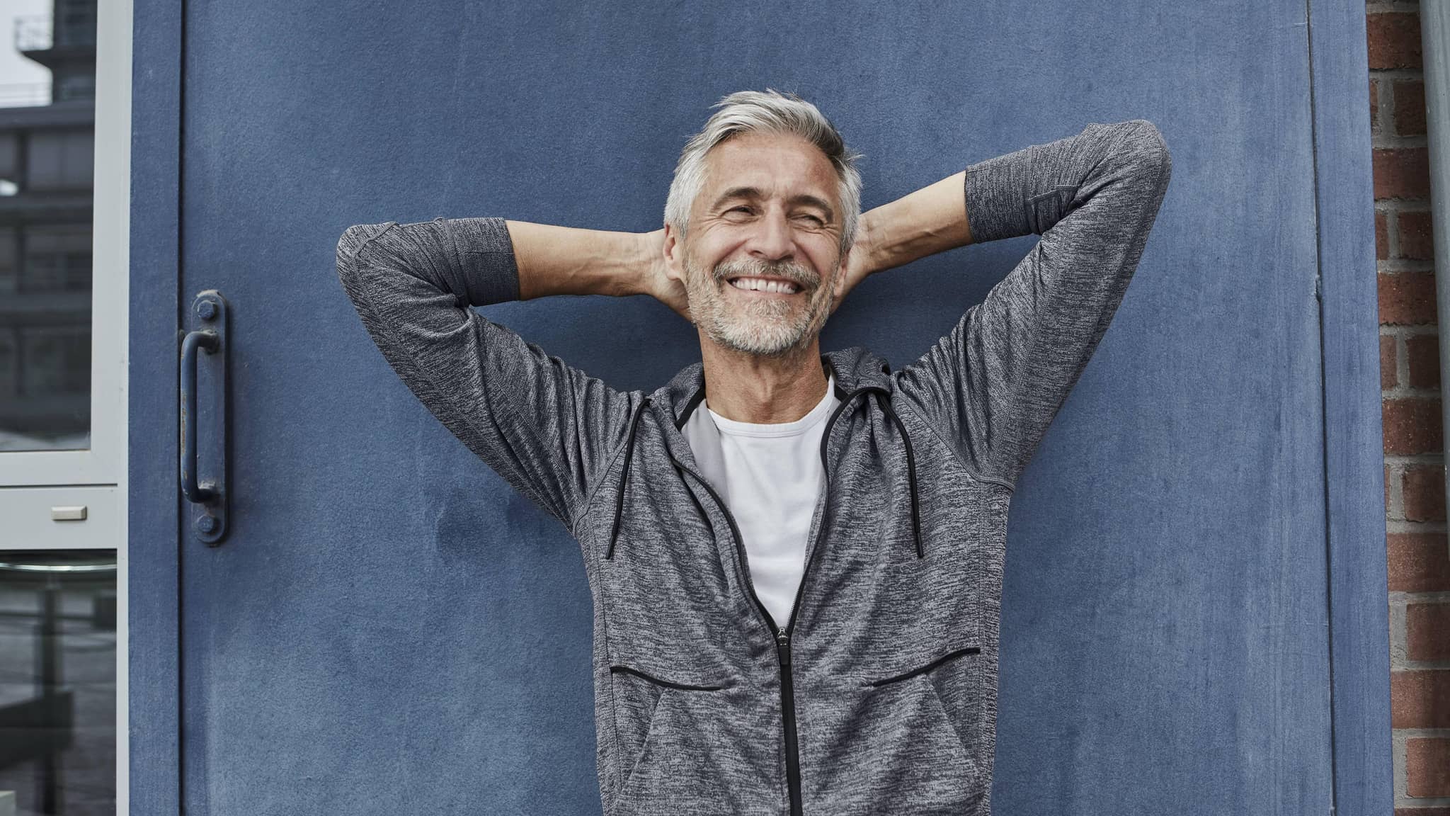 Portrait eines lachenden grauhaarigen Mannes vor einer blauen Tür