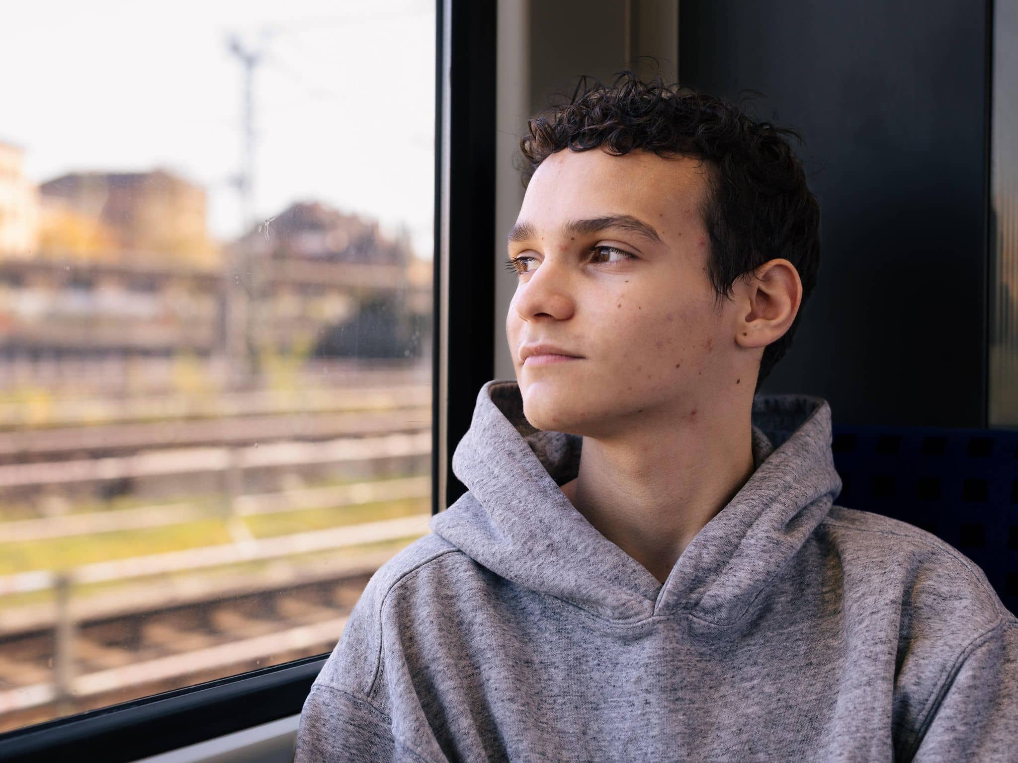 Jugendlicher blickt mit ernstem Gesicht aus einem Zugfenster
