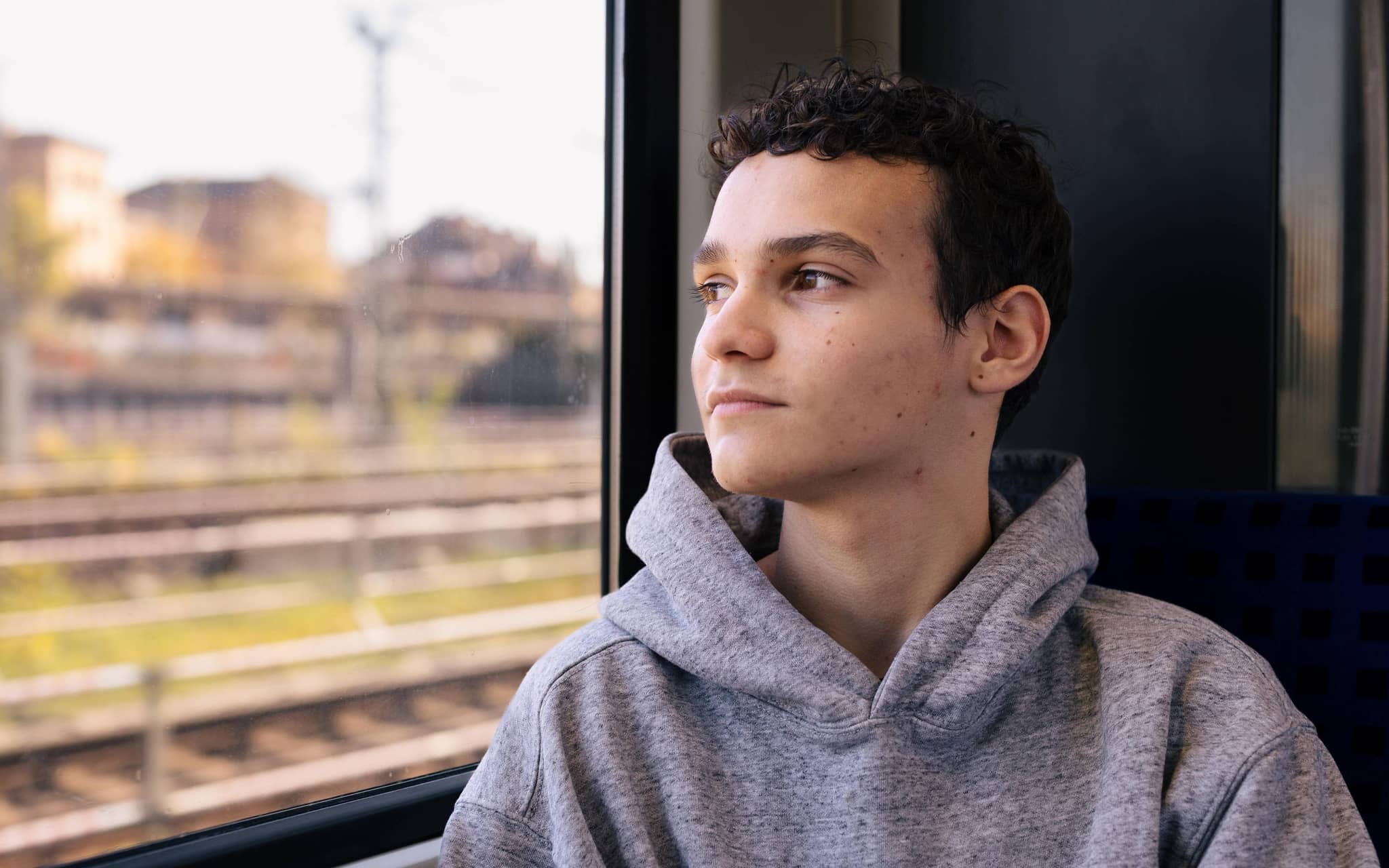 Jugendlicher blickt mit ernstem Gesicht aus einem Zugfenster
