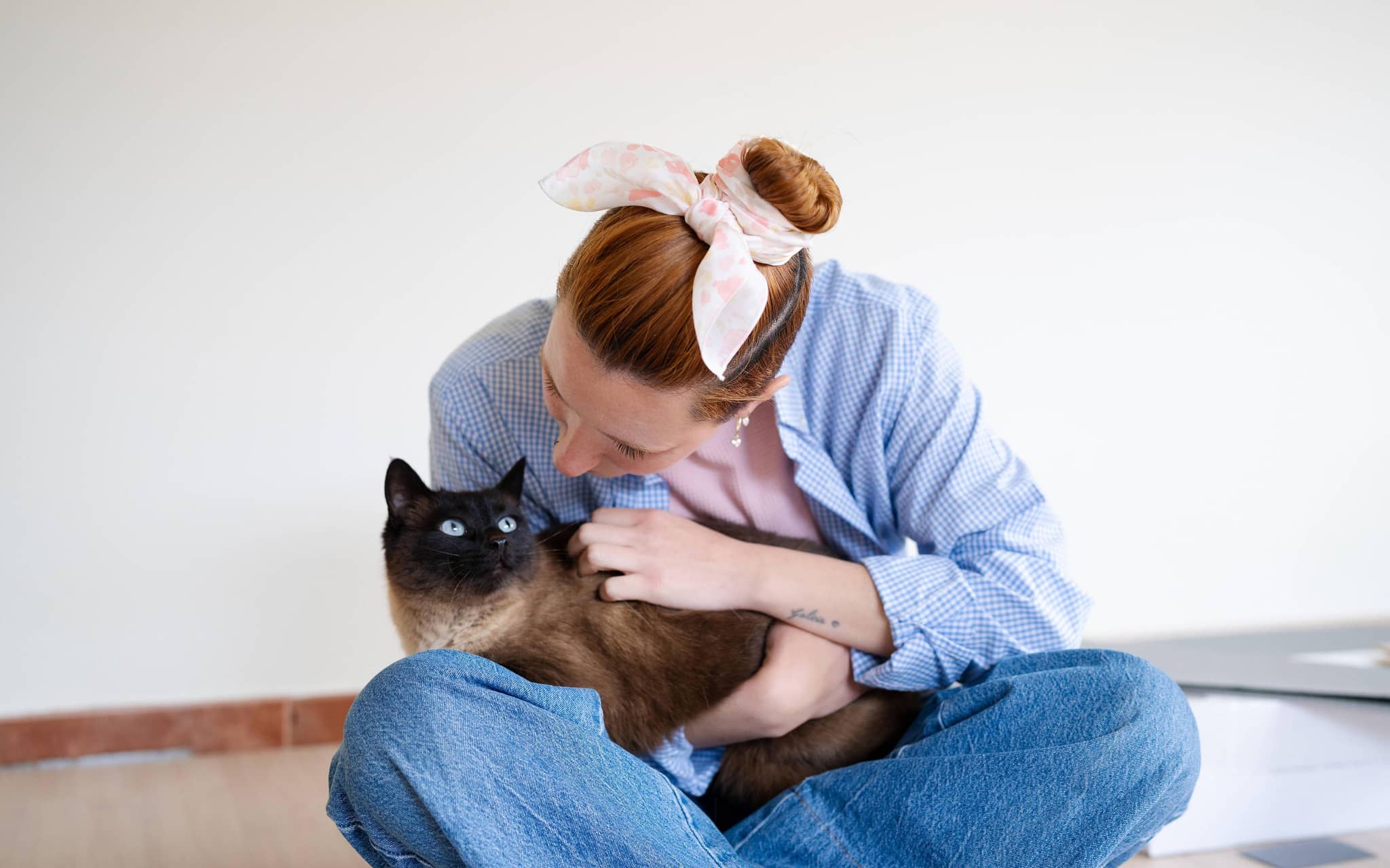 Frau im Schneidersitz hält Katze auf dem Schoß und blickt ihr ins Gesicht.