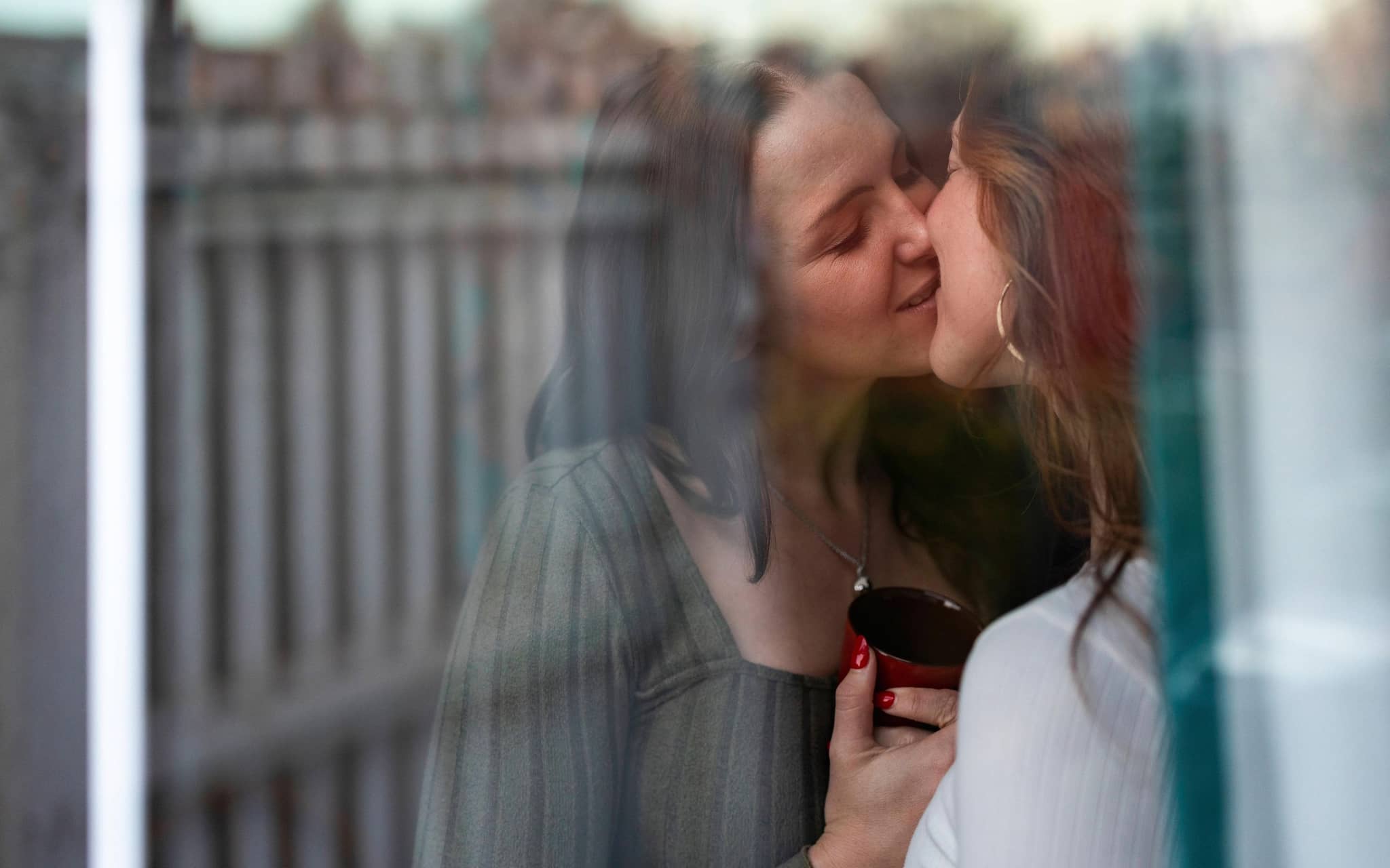 Zwei junge Frauen stehen am Fenster und küssen sich