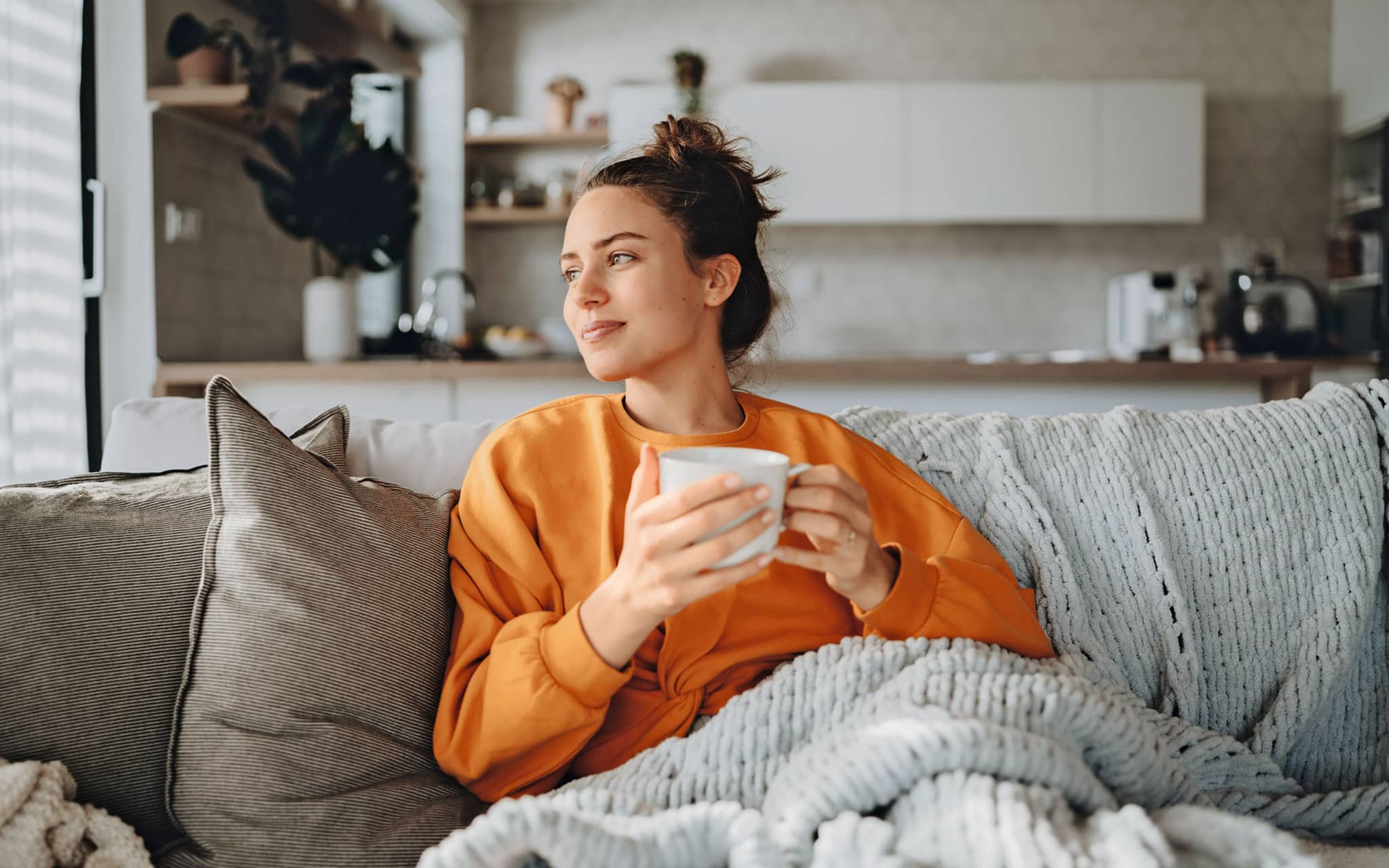 Bild: Junge Frau sitzt mit einer Decke und einer Tasse Tee auf der Couch.