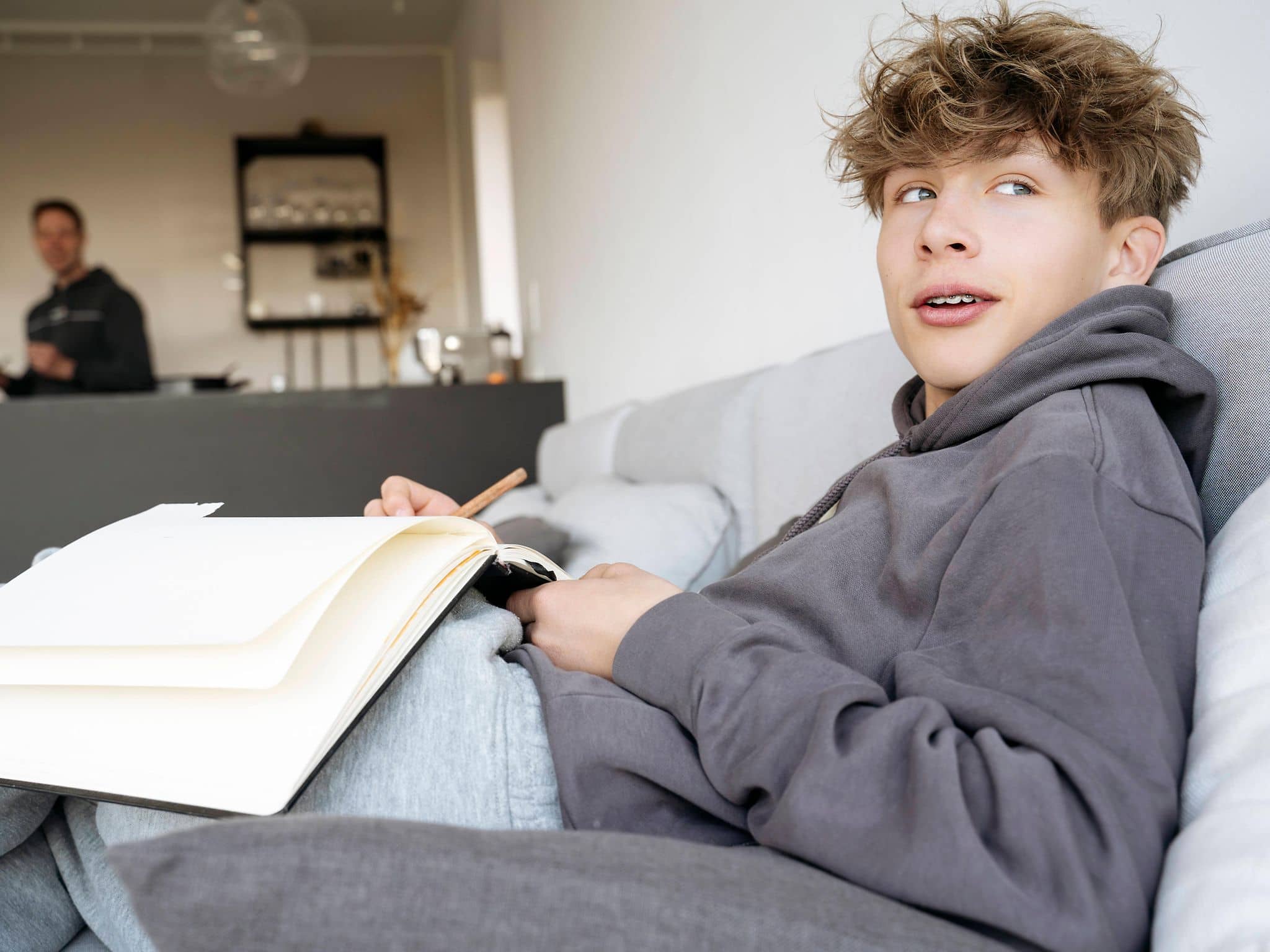 Jugendlicher sitzt auf dem Sofa und hält ein Notizbuch in der Hand