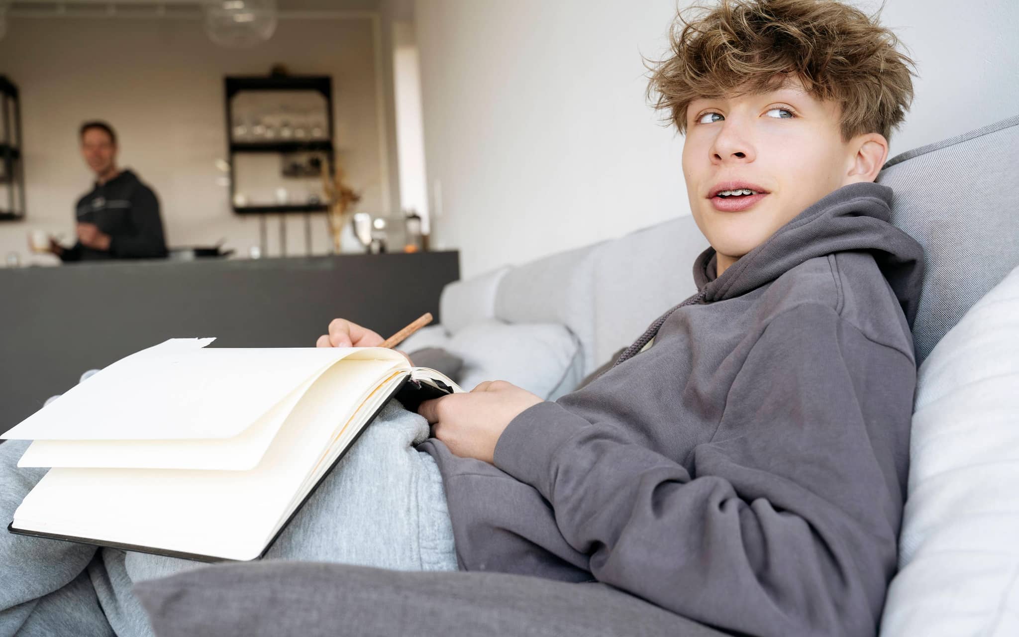 Jugendlicher sitzt auf dem Sofa und hält ein Notizbuch in der Hand