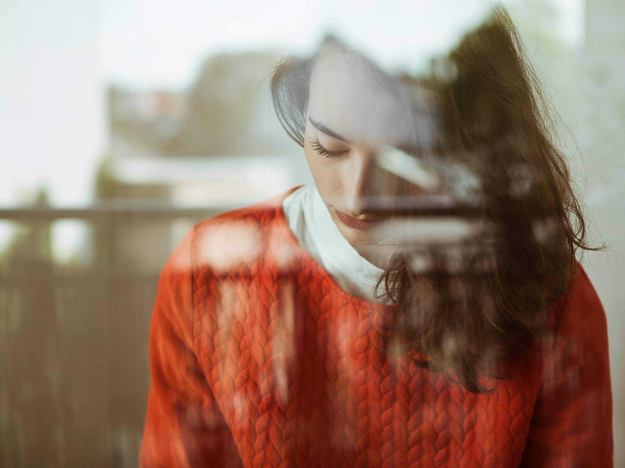 Junge Frau mit gesenktem Blick hinter einem Fenster.