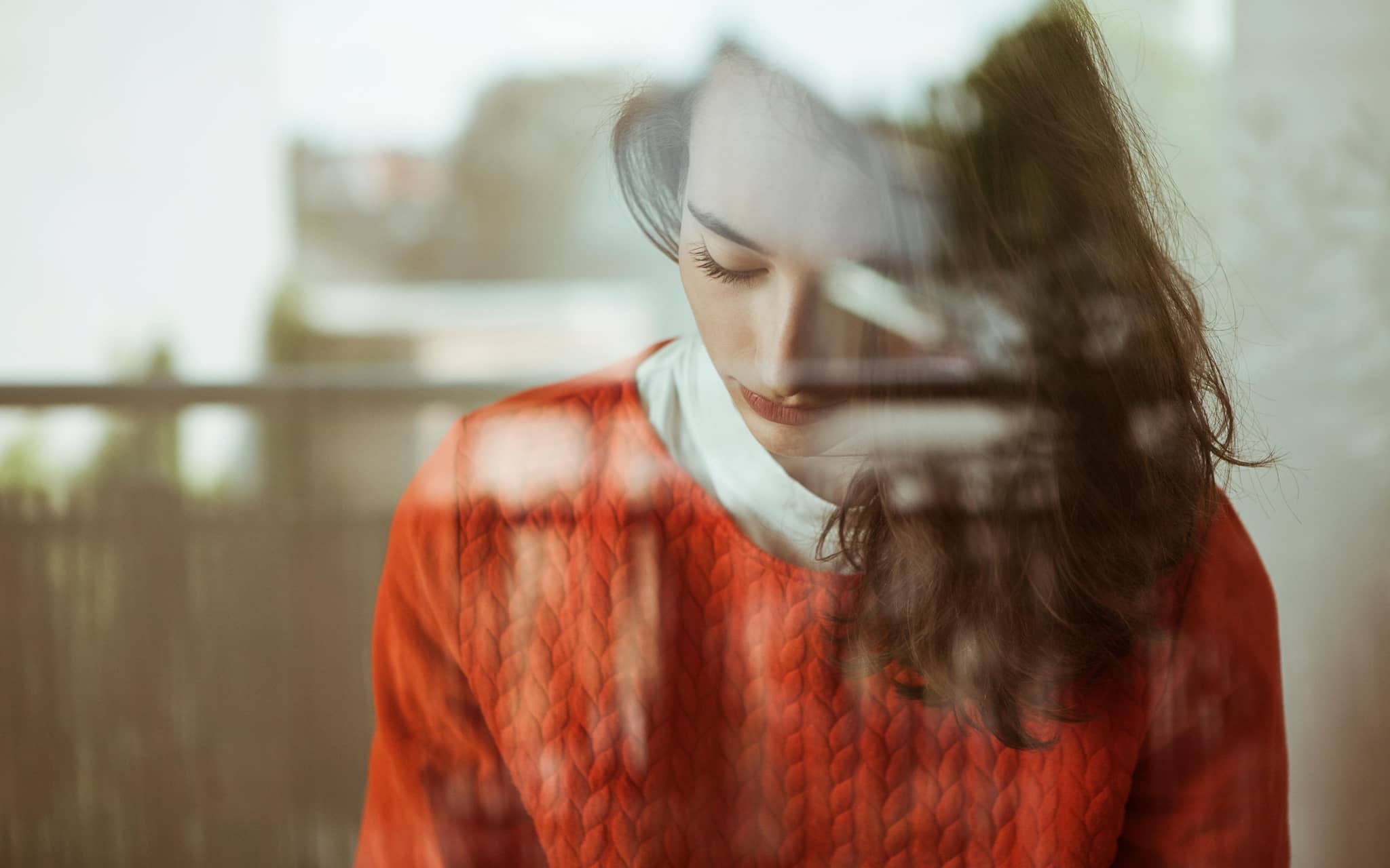Junge Frau mit gesenktem Blick hinter einem Fenster.