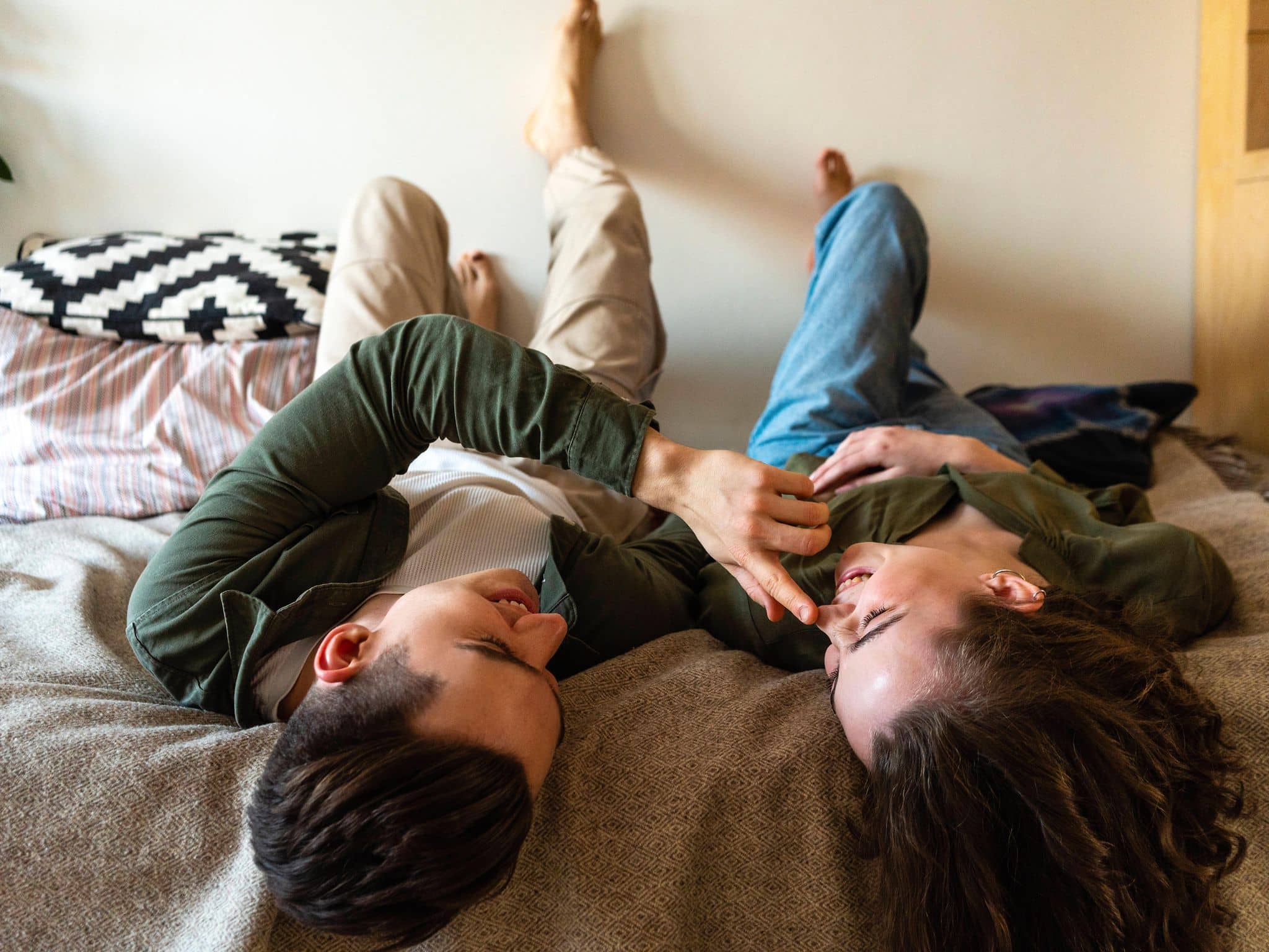 Mann berührt Nase seiner Freundin, die neben ihm im Bett liegt