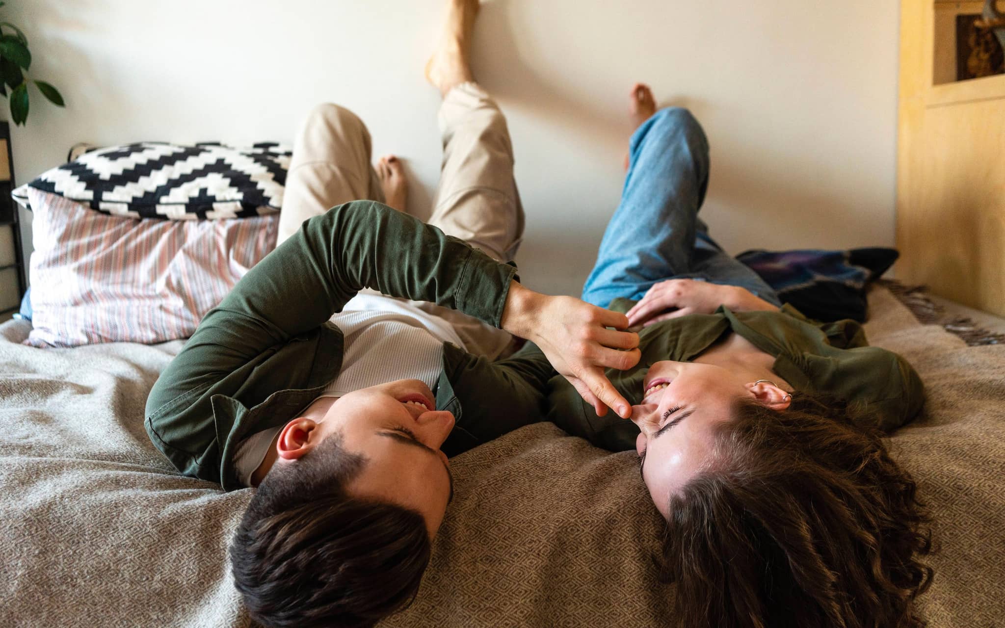 Mann berührt Nase seiner Freundin, die neben ihm im Bett liegt