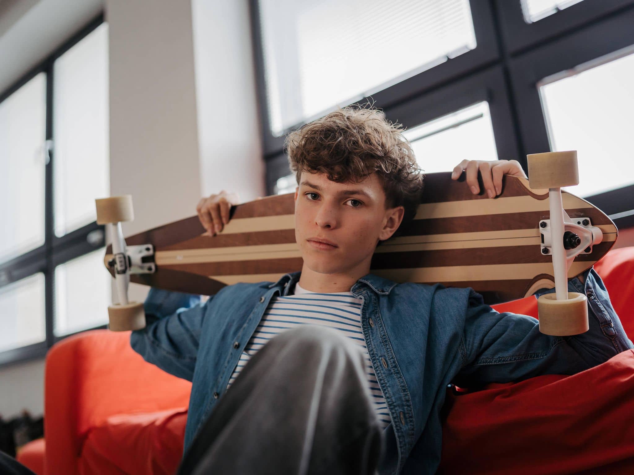Junge blickt in die Kamera und hält ein Longboard über seinen Schultern