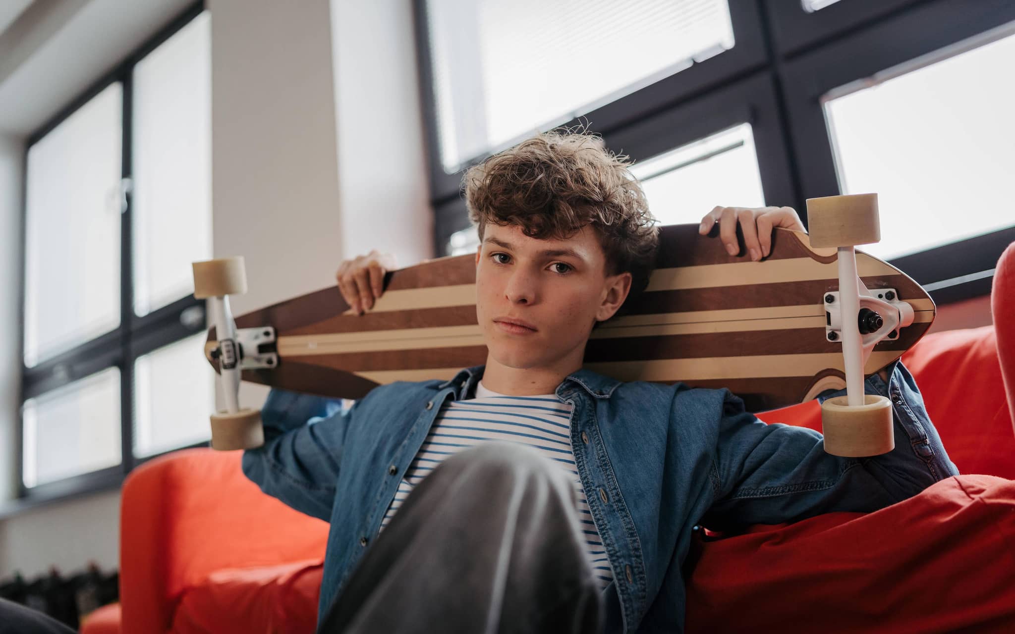 Junge blickt in die Kamera und hält ein Longboard über seinen Schultern