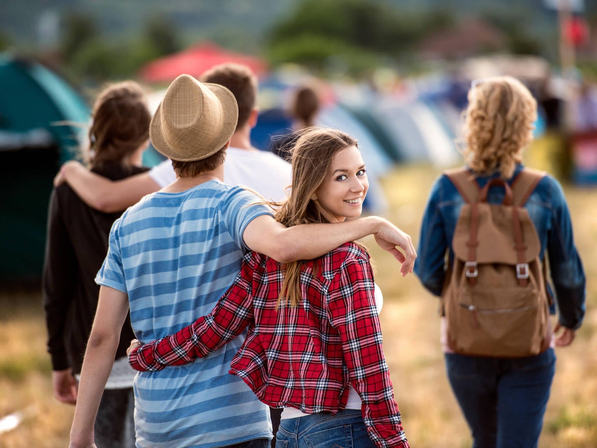 Junge Frau läuft Arm in Arm mit einem Mann über einen Zeltplatz