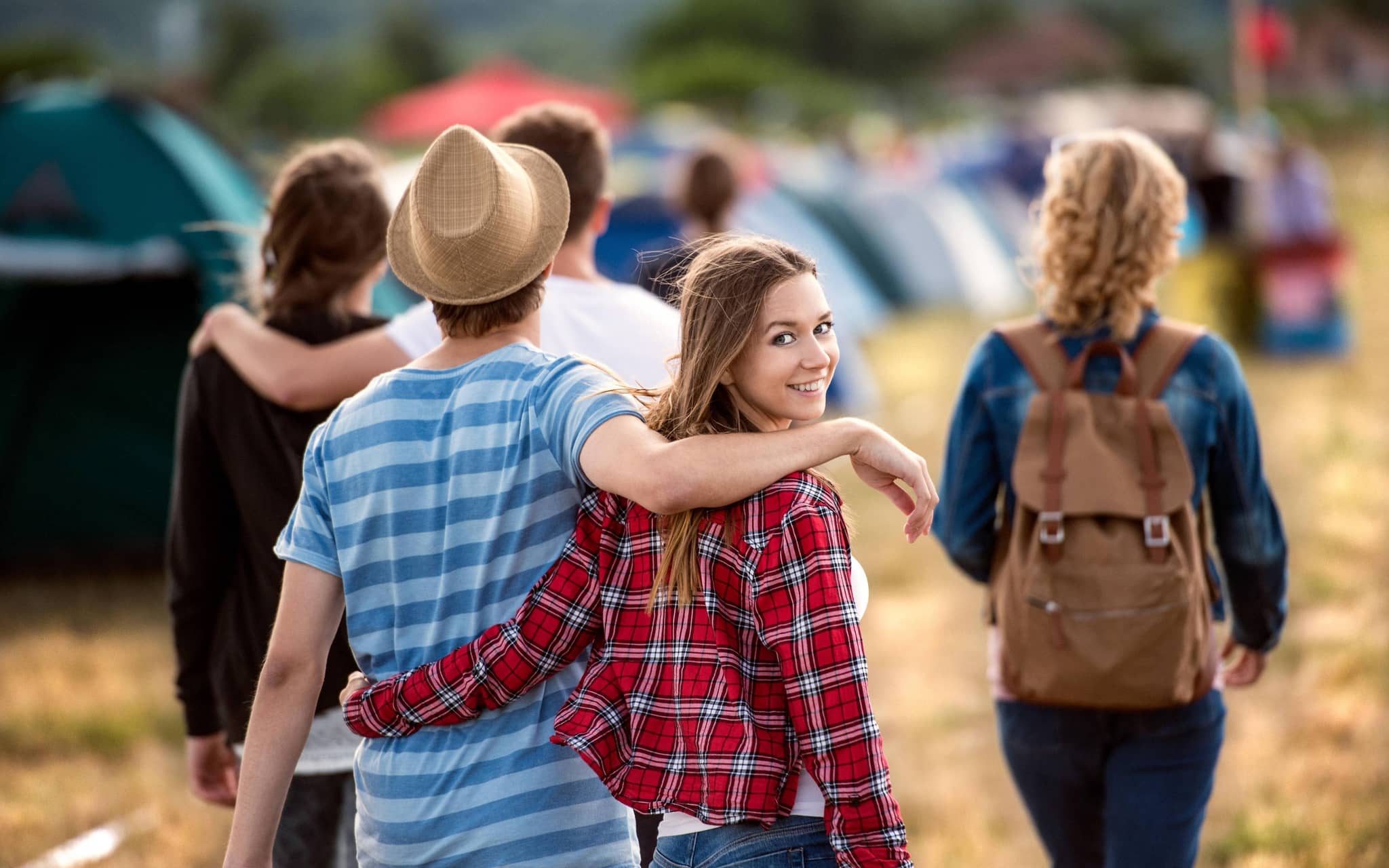 Junge Frau läuft Arm in Arm mit einem Mann über einen Zeltplatz
