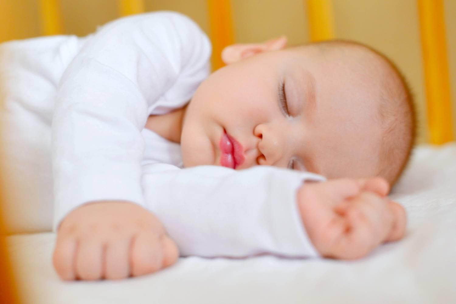 Neurodermitis-Overalls: Baby trägt weiße langärmelige Kleidung und schläft zufrieden in seinem Bett.