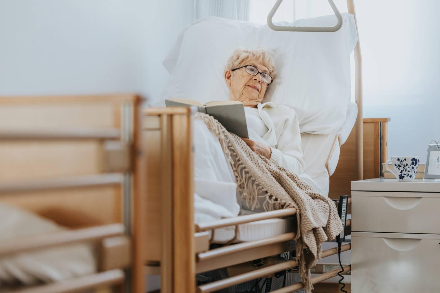 Pflegebetten: Ältere Frau liegt in einem Pflegebett und liest ein Buch.