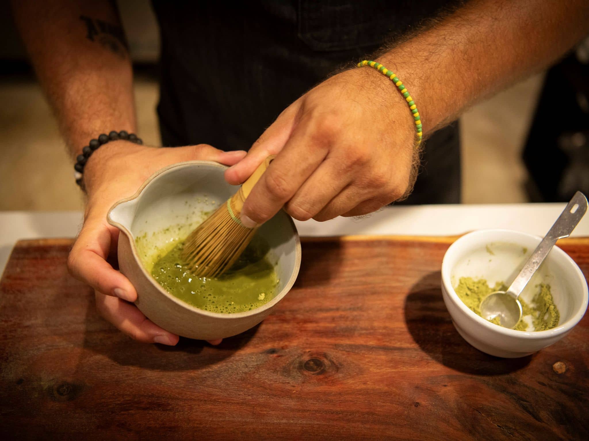 Nahaufnahme zweier Hände eines Manns, der mit einem Matchabesen grünen Matcha anrührt.