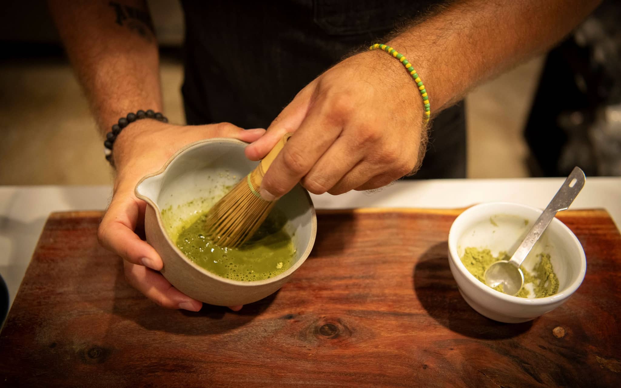 Nahaufnahme zweier Hände eines Manns, der mit einem Matchabesen grünen Matcha anrührt.