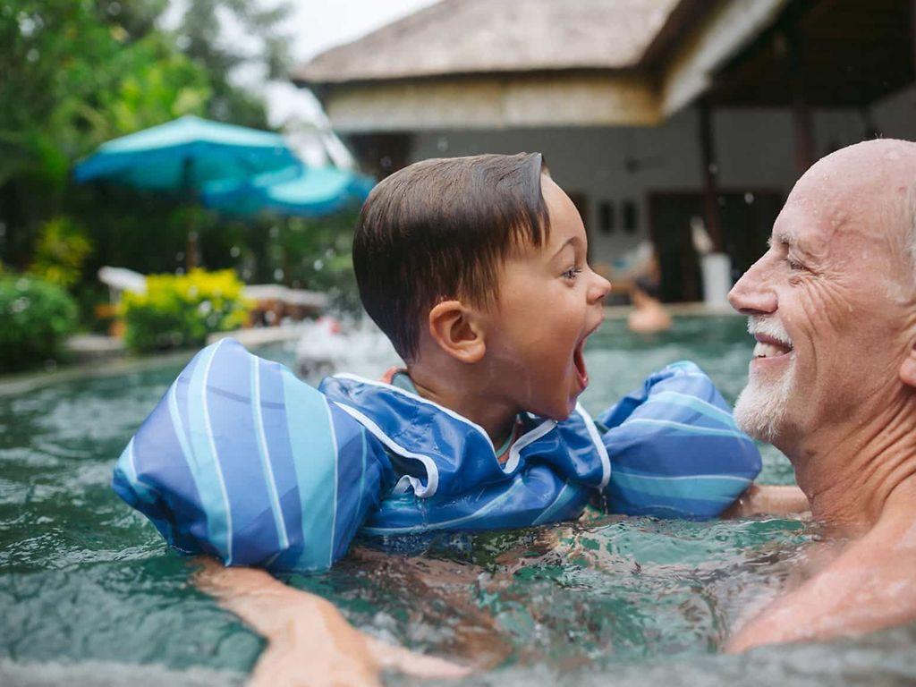 Herzinsuffizienz: Älterer Mann und kleiner Junge haben Spaß im Wasser.