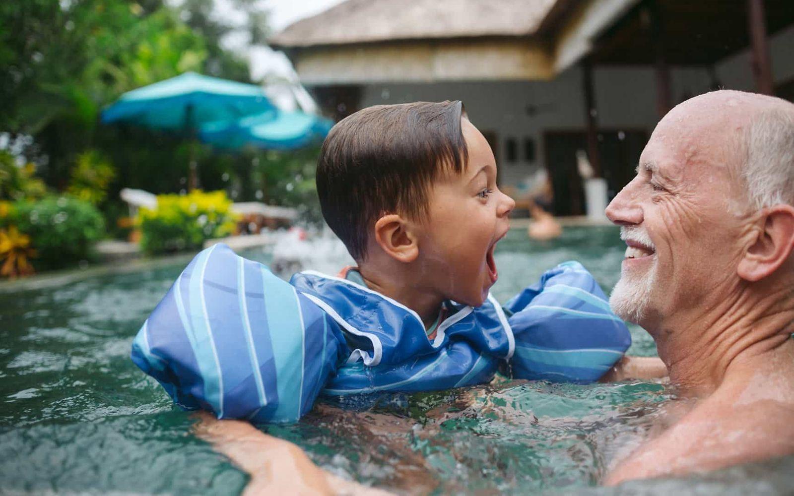 Herzinsuffizienz: Älterer Mann und kleiner Junge haben Spaß im Wasser.