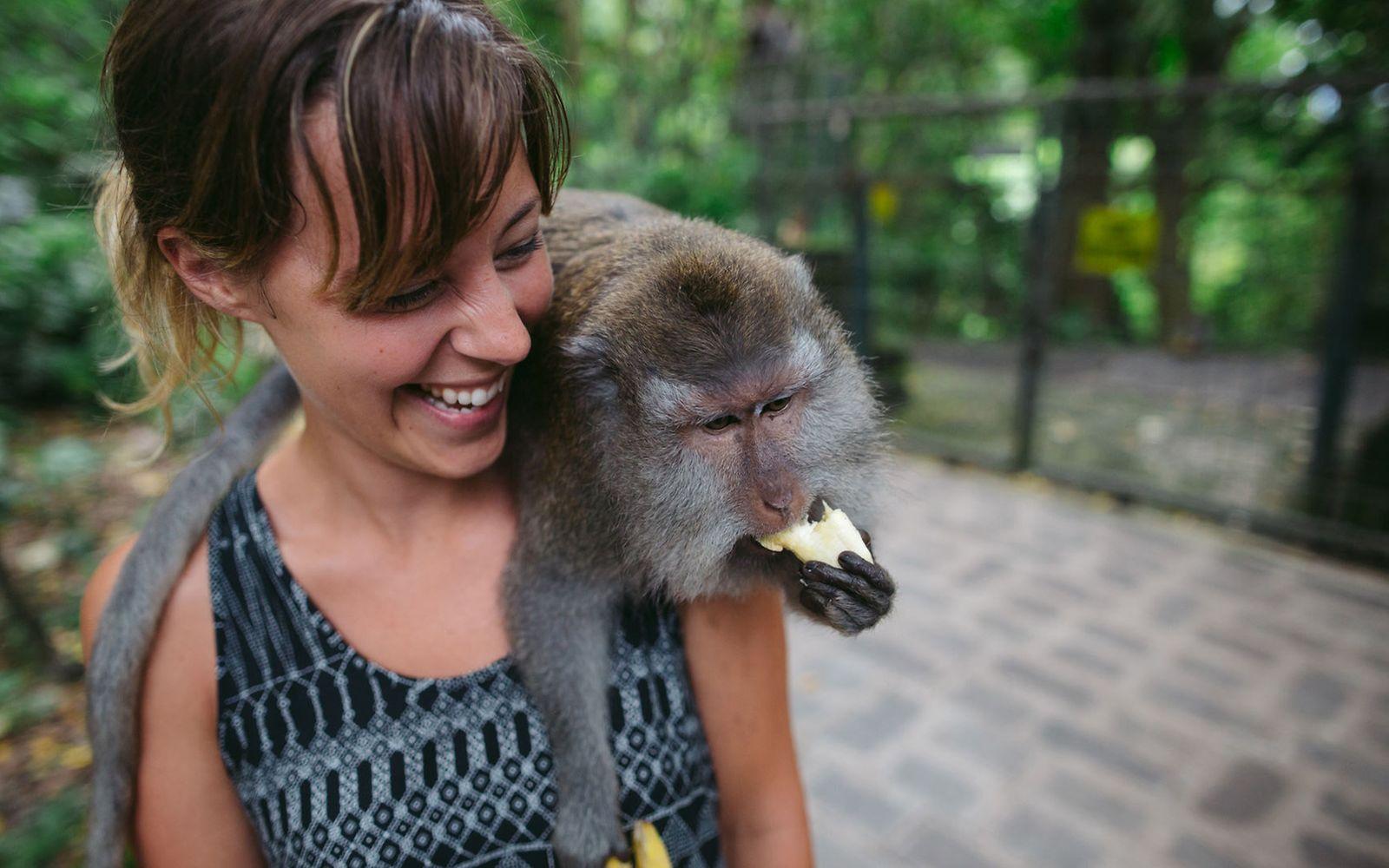 Krankenversicherung im Ausland: Frau mit Affen auf der Schulter hat Spaß.