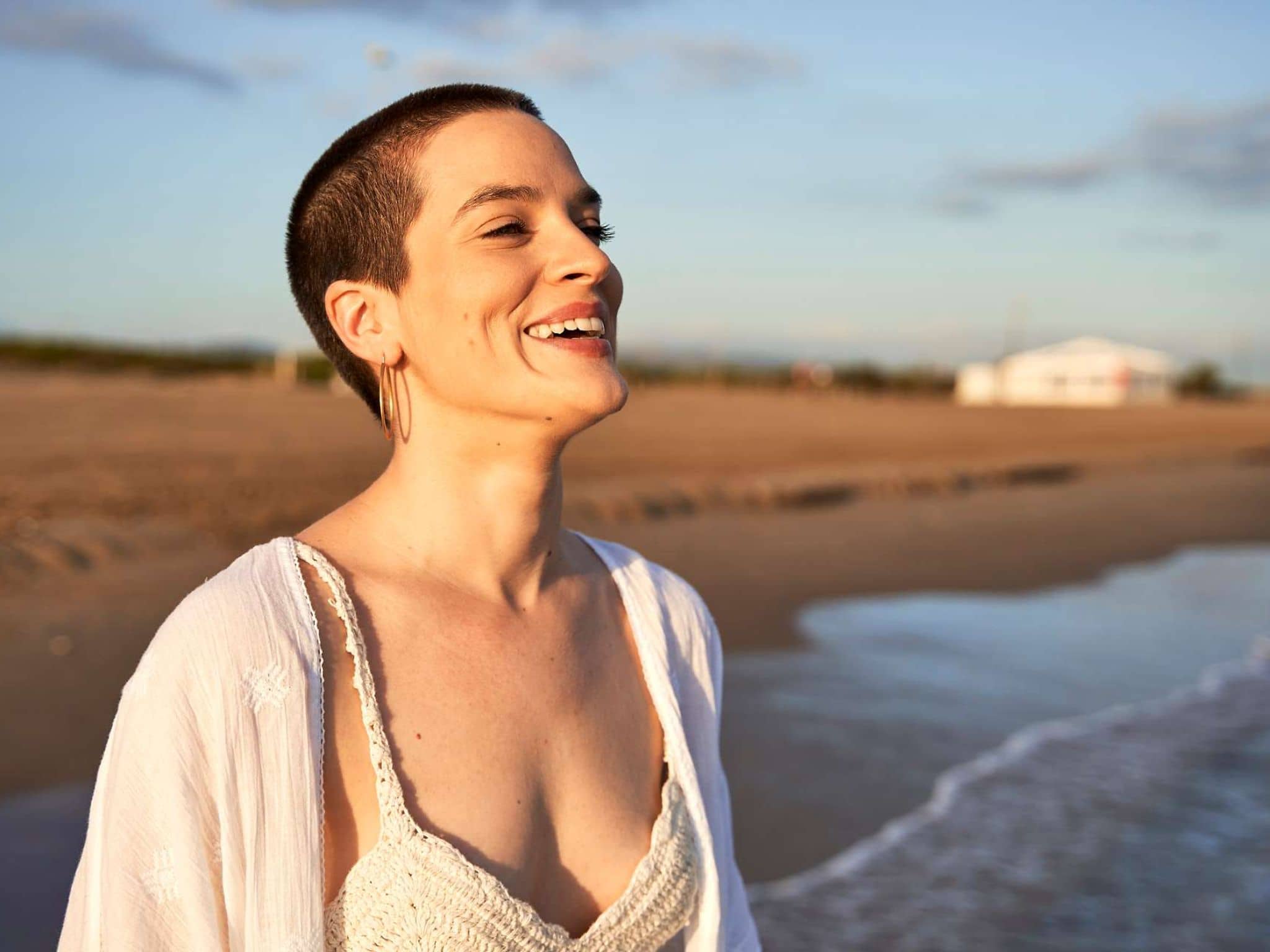 Frau steht am Strand und schaut fröhlich aufs Meer.