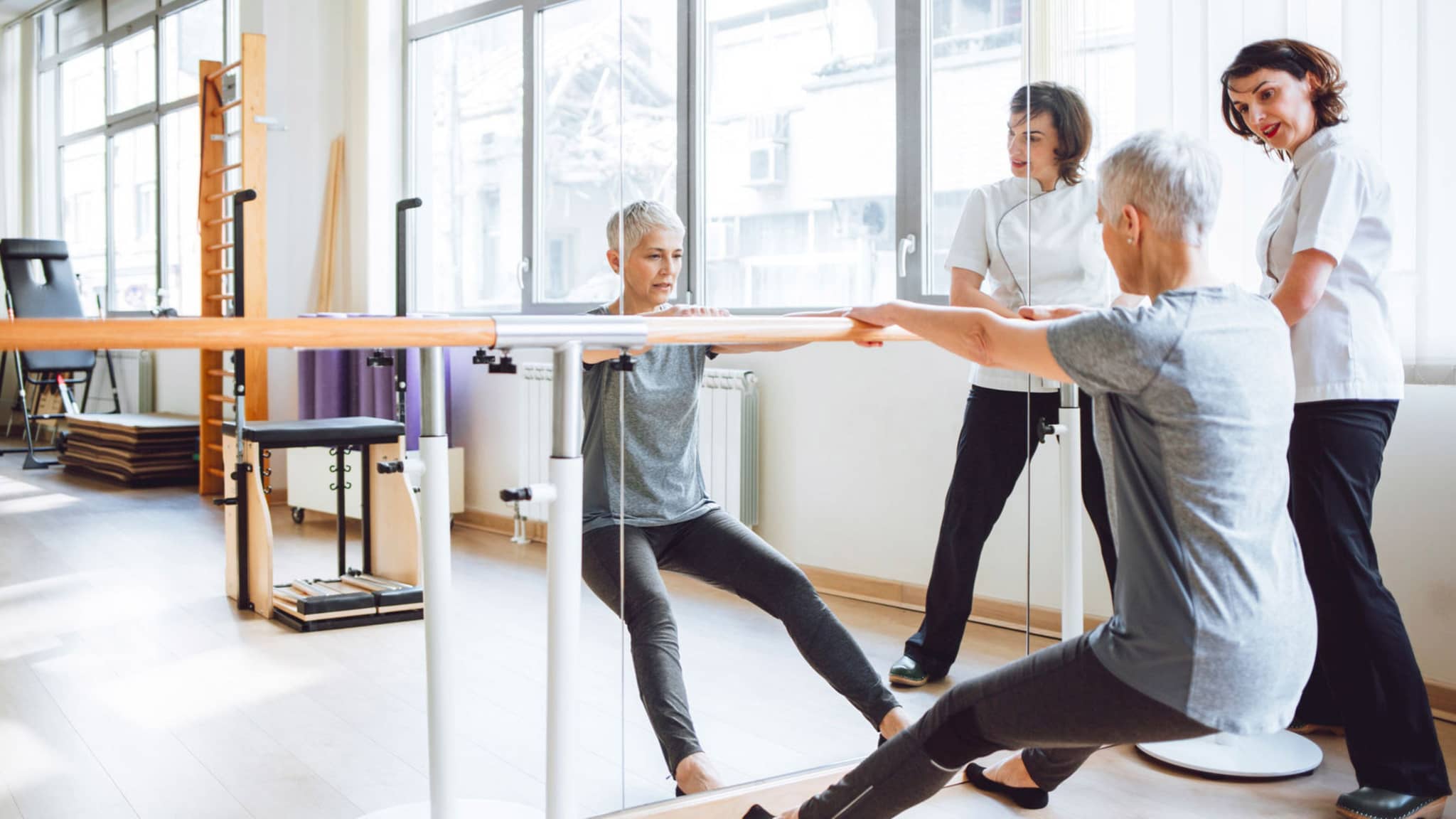 Rehasport: Frau und Trainerin an Stange am Spiegel.