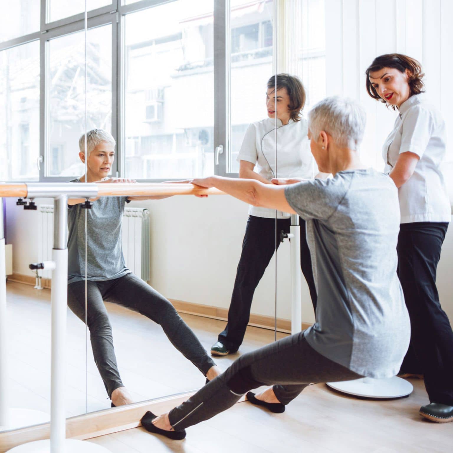 Rehasport: Frau und Trainerin an Stange am Spiegel.