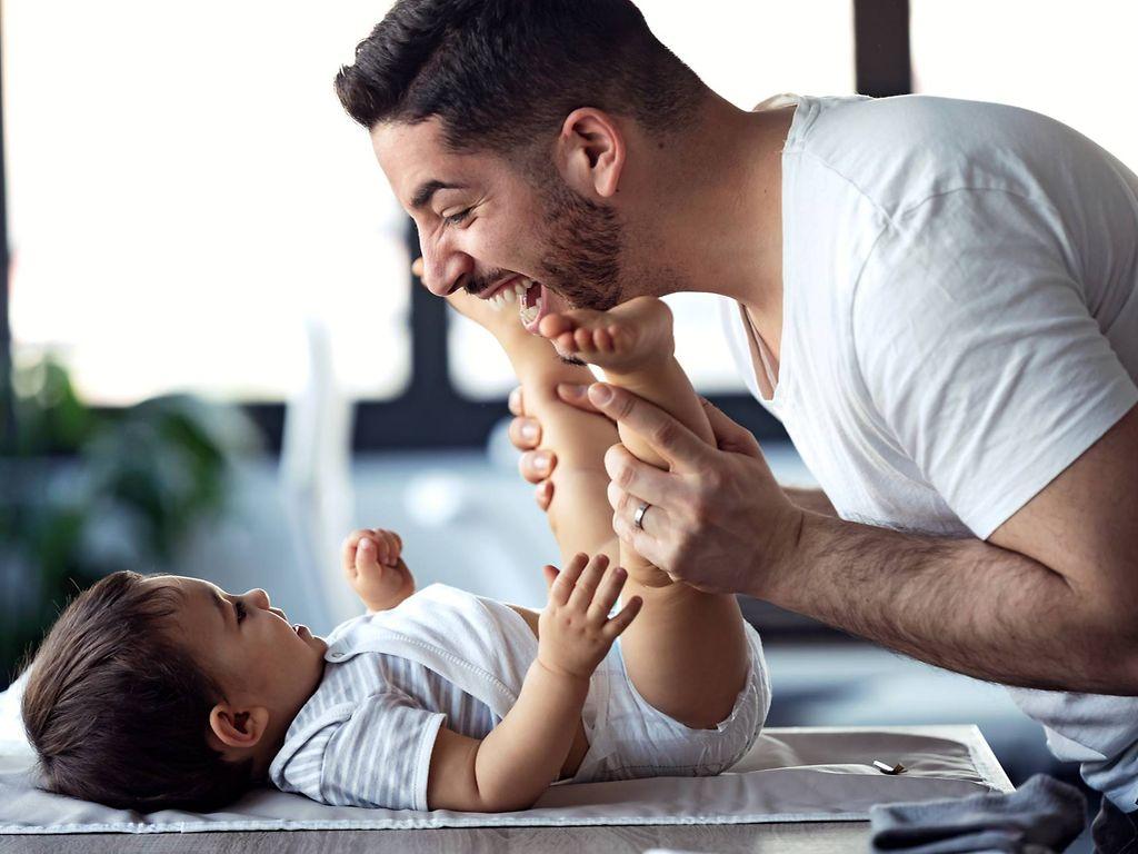 U5 Vorsorgeuntersuchung: Vater lacht und spielt mit seinem Baby beim Windelwechsel 