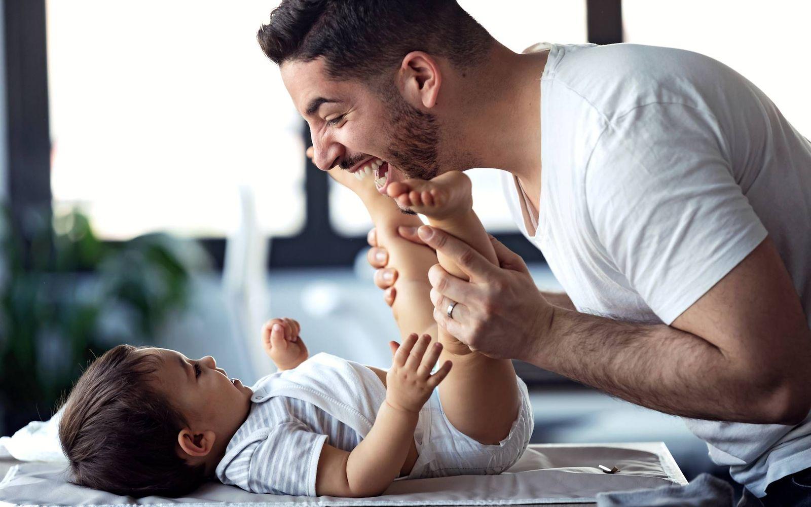 U5 Vorsorgeuntersuchung: Vater lacht und spielt mit seinem Baby beim Windelwechsel 