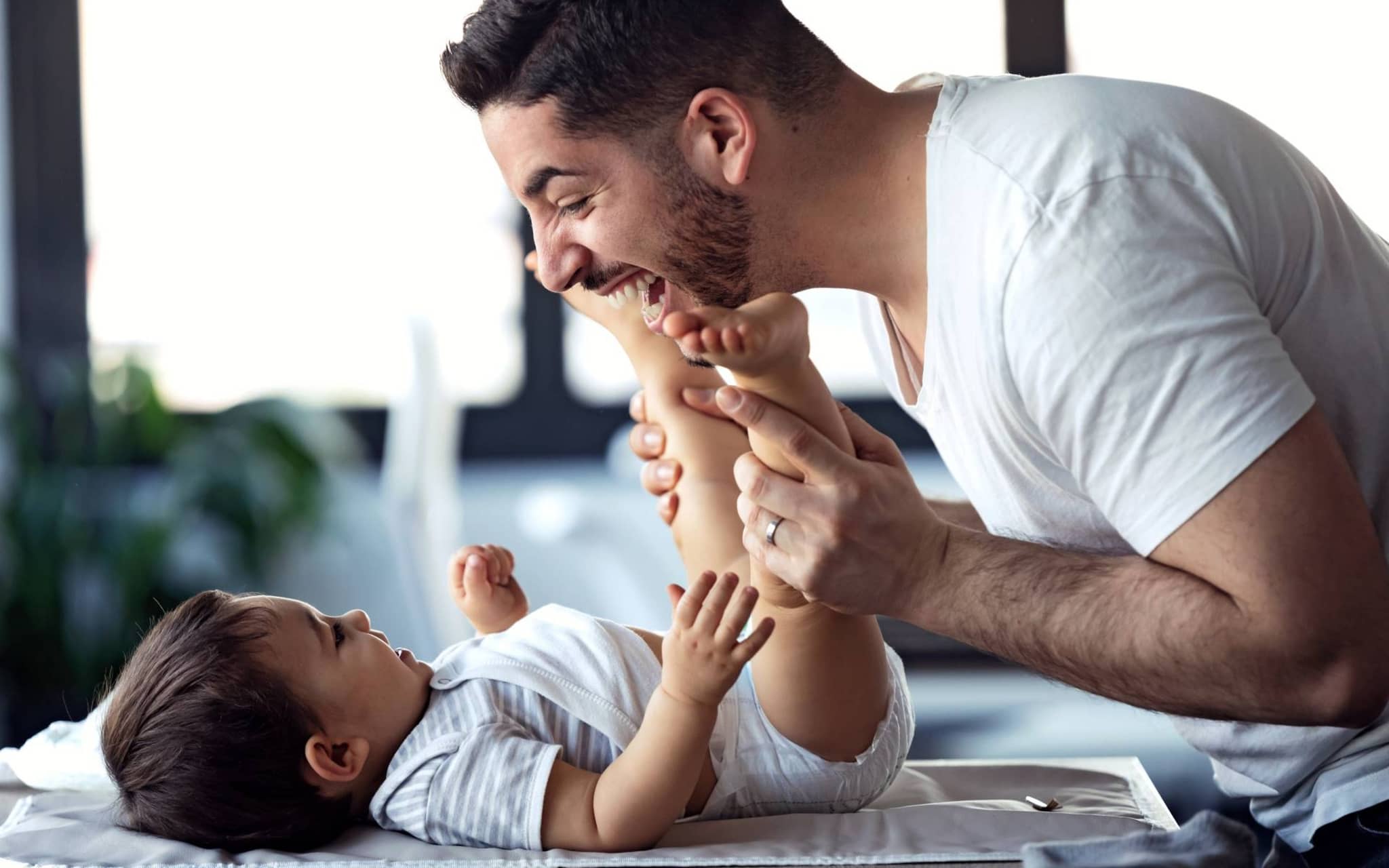 U5 Vorsorgeuntersuchung: Vater lacht und spielt mit seinem Baby beim Windelwechsel