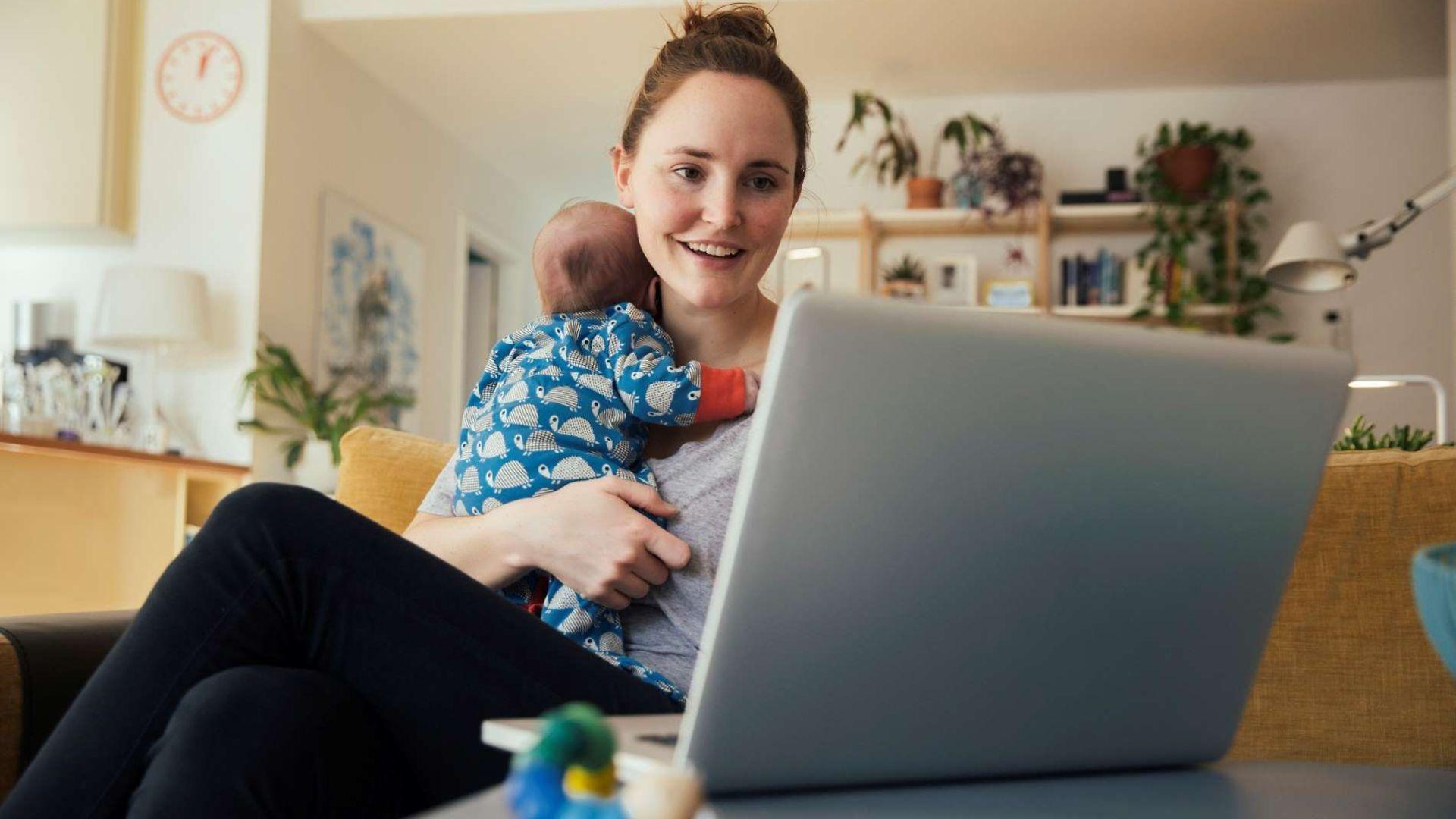 Online-Seminare: Frau mit Baby auf dem Arm schaut auf ein Notebook.