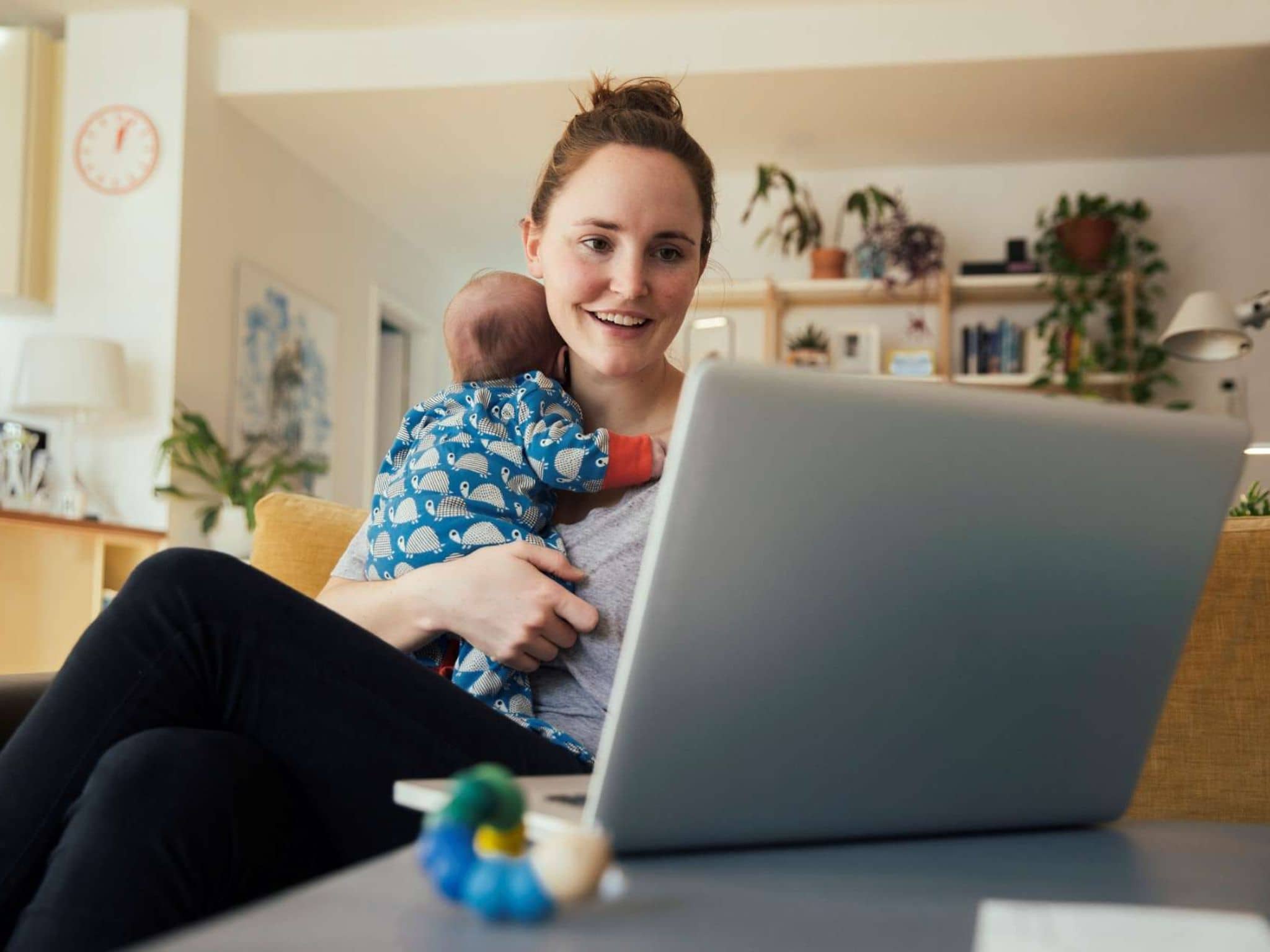 Online-Seminare: Frau mit Baby auf dem Arm schaut auf ein Notebook.