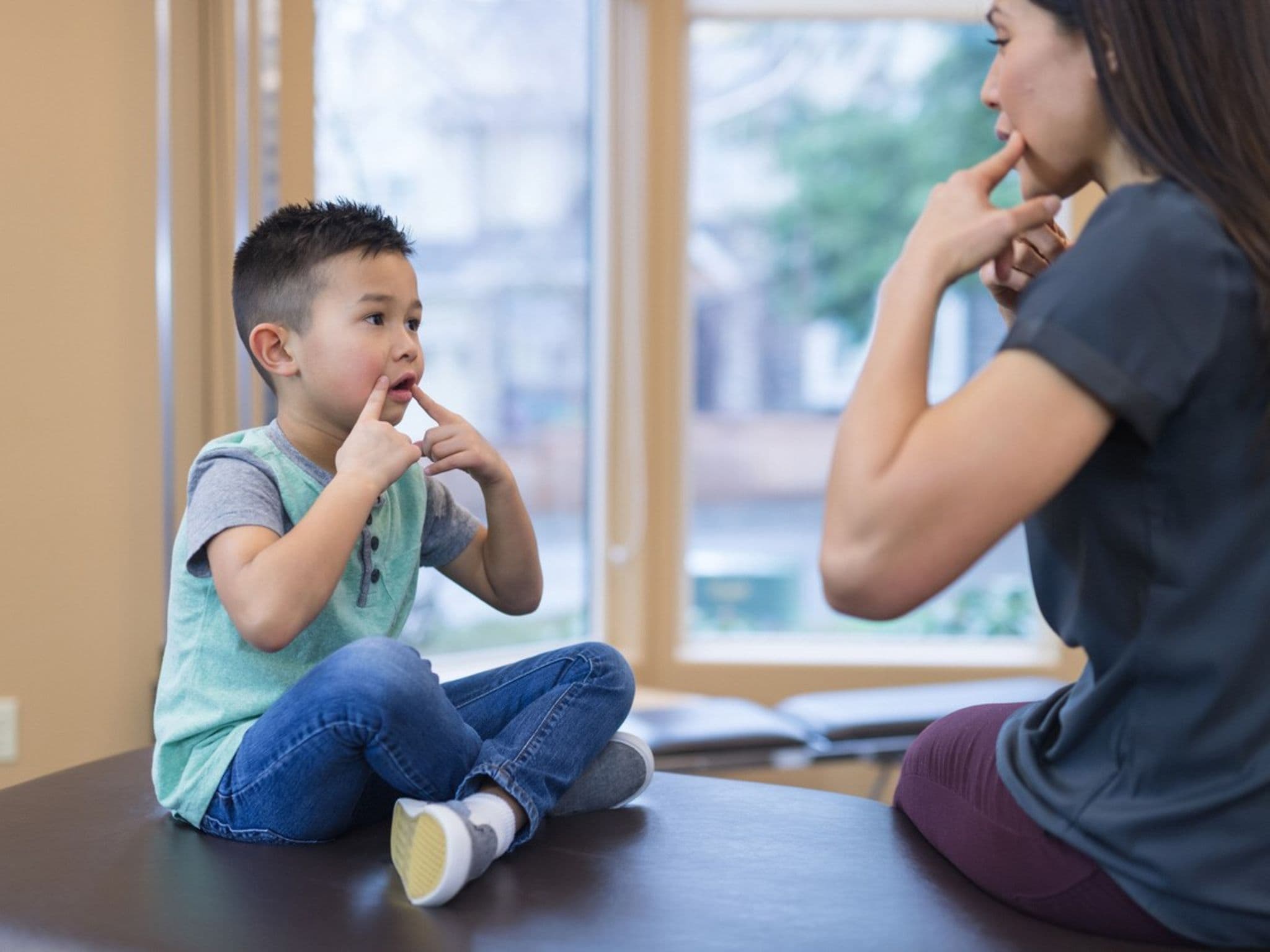 Logopädie: Eine junge Frau übt mit einem gegenüber sitzenden Kind sprechen.