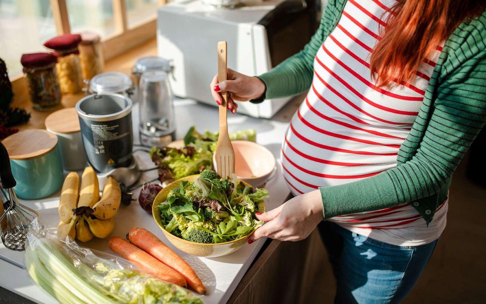 Schwangere Frau bereitet Salat in der Küche zu