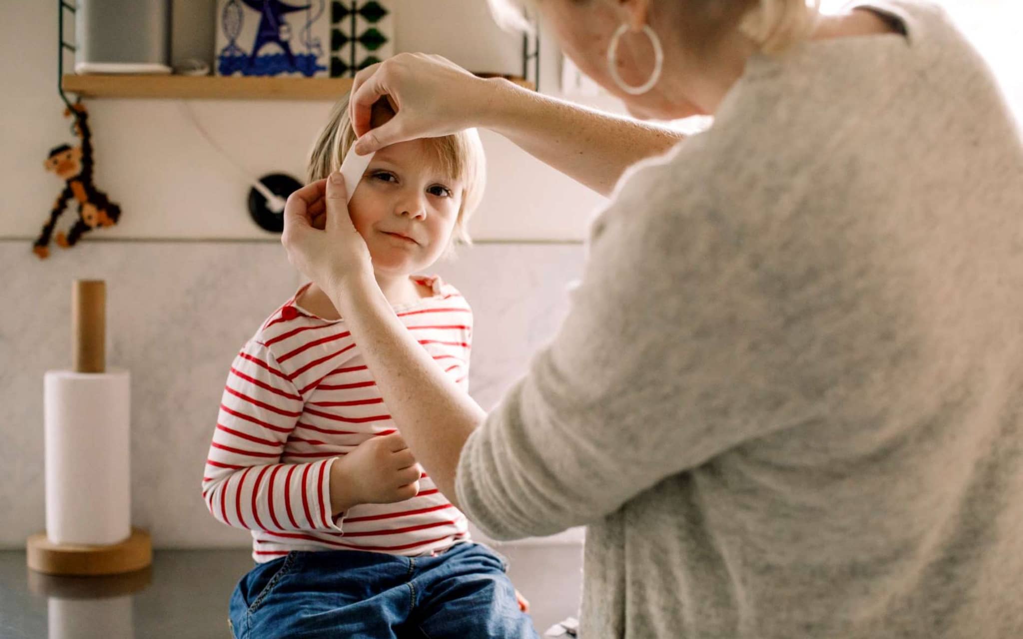 Erste Hilfe am Kind: Mutter klebt Pflaster auf die Schläfe ihres Kindes