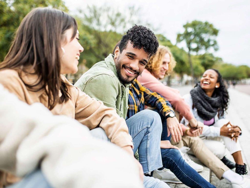 Eine Gruppe junger Leute sitzt im Freien und lacht miteinander