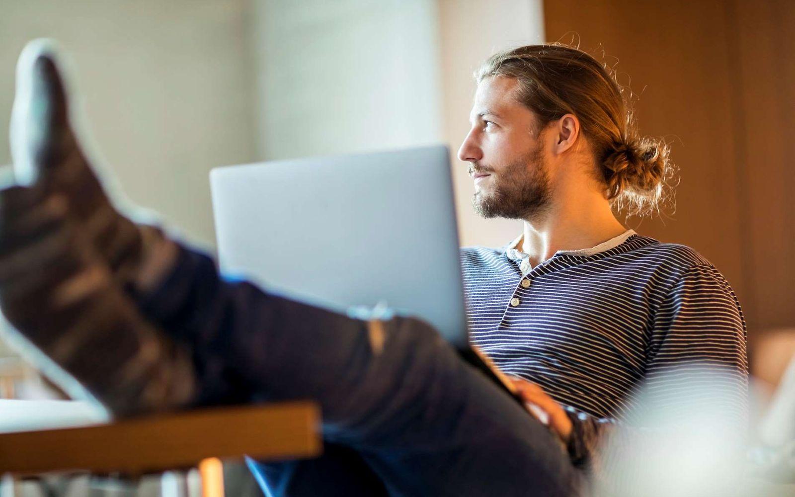 Work-Live-Balance: Mann sitzt in entspannter Pose mit Laptop auf dem Schoß