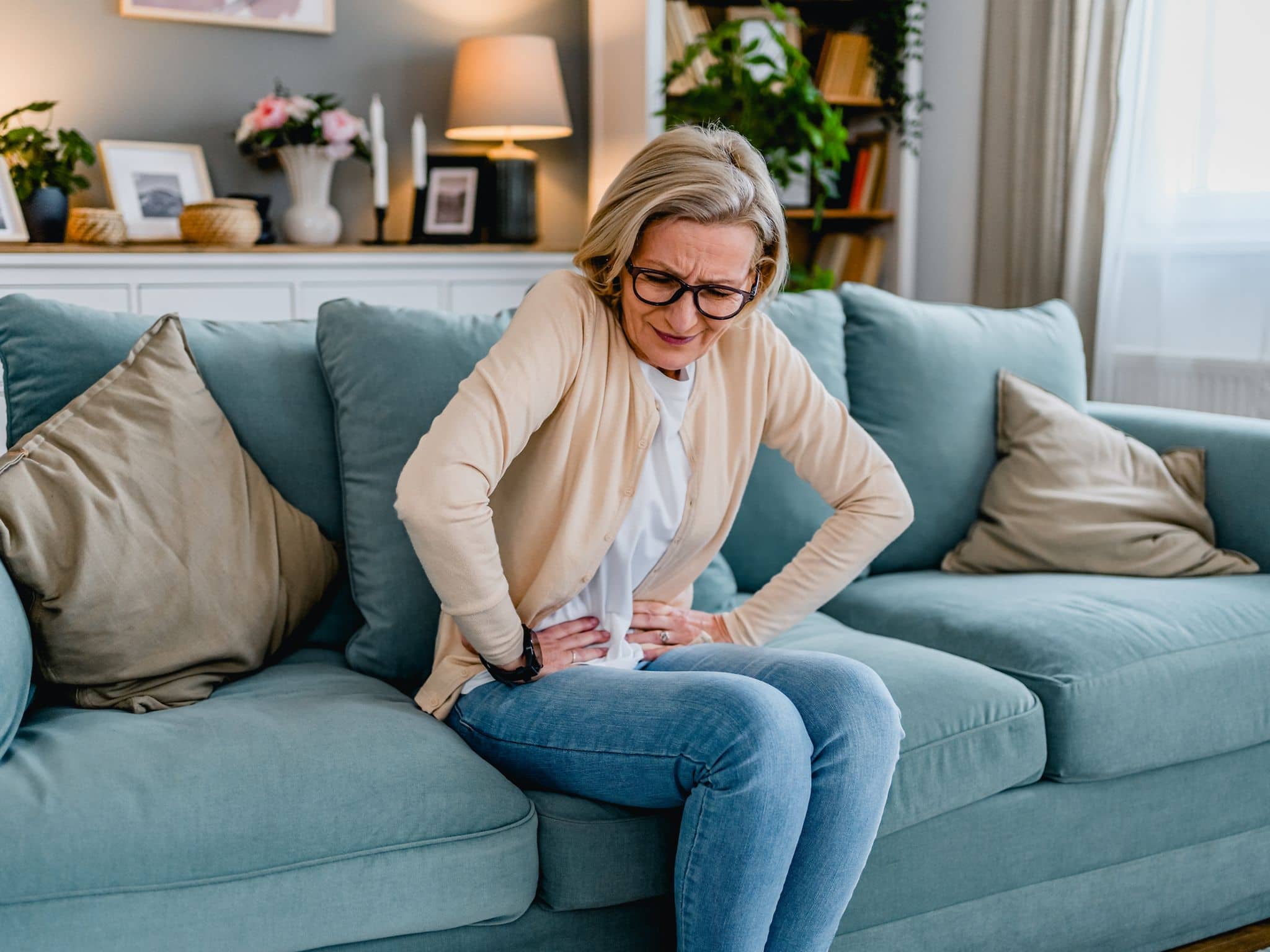Verstopfung: Eine ältere Frau sitzt gekrümmt auf dem Sofa und hält sich ihren Bauch