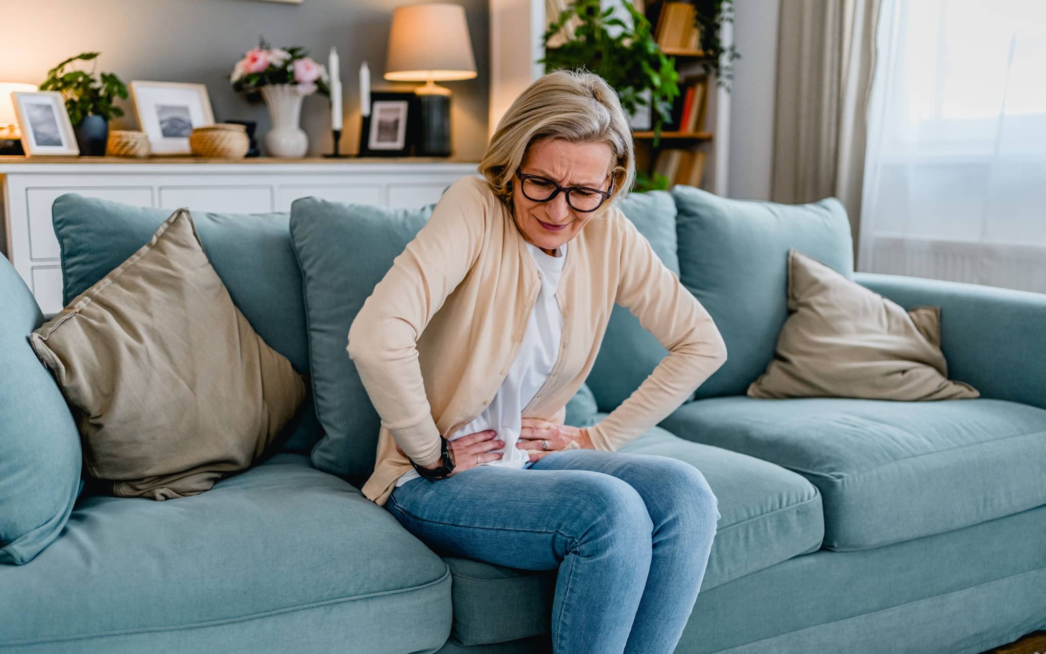 Verstopfung: Eine ältere Frau sitzt gekrümmt auf dem Sofa und hält sich ihren Bauch