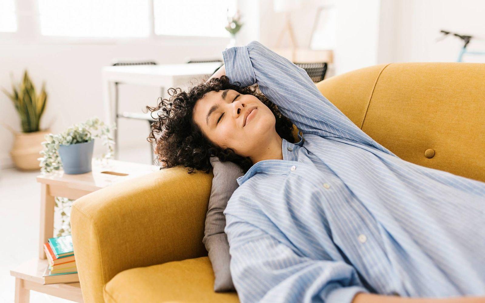 Stressmanagement: Lächelnde Frau liegt entspannt mit geschlossenen Augen auf der Couch.