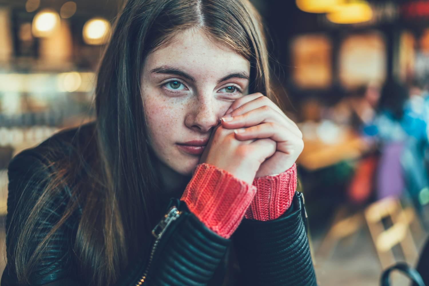 Mädchen im Teenager-Alter sitzt in einem Café und schaut verträumt in den Raum.