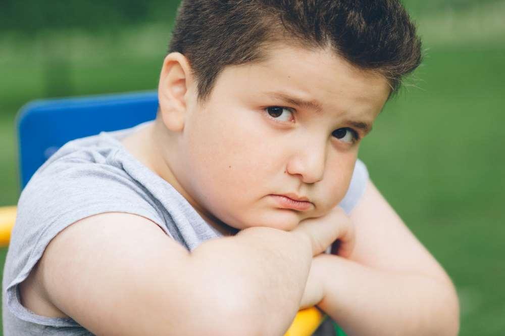 Circa zehn Jahre alter Junge mit leichtem Übergewicht schaut traurig in die Kamera.