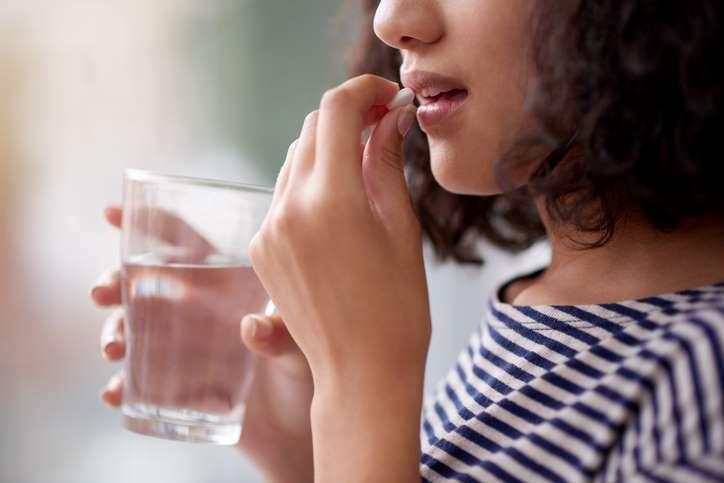 Mädchen hält ein Glas Wasser in der Hand und steckt sich eine Tablette in den Mund.