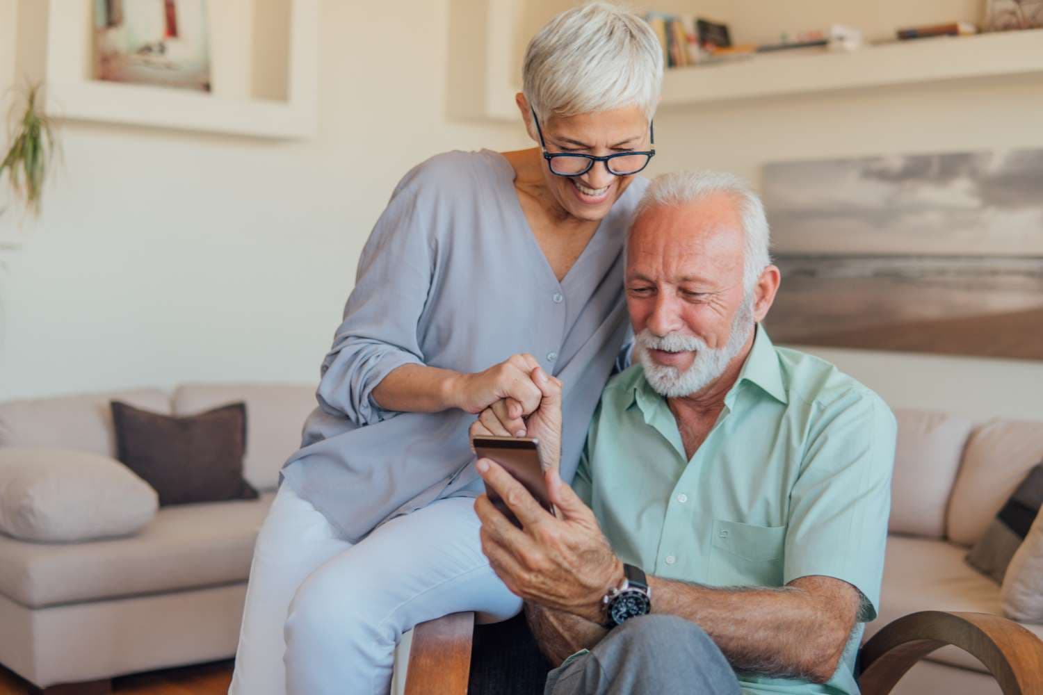Hilfsmittel-Antrag: Älteres Paar sitzt auf dem Sofa und schaut gemeinsam auf ein Smartphone.