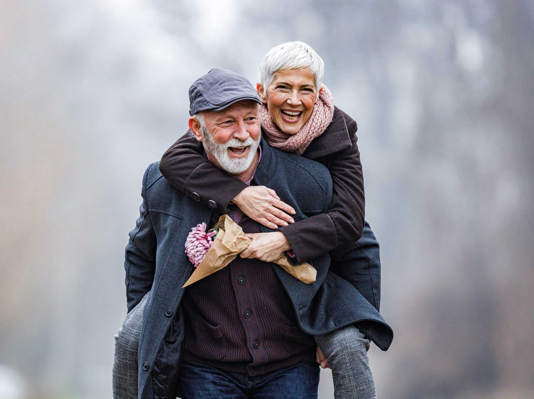 Ein vergnügtes älteres Paar, das sich im Winter im Park huckepack nimmt.