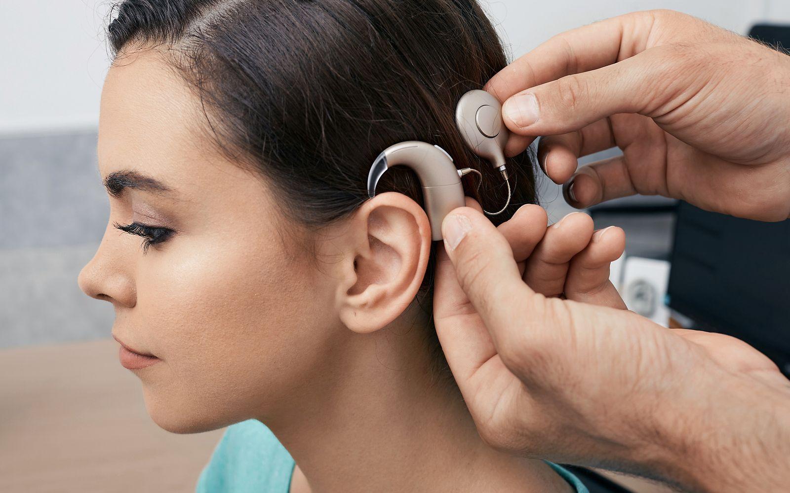 Abbildung einer jungen Frau, der das Cochlea Implantat am Ohr angebracht wird.